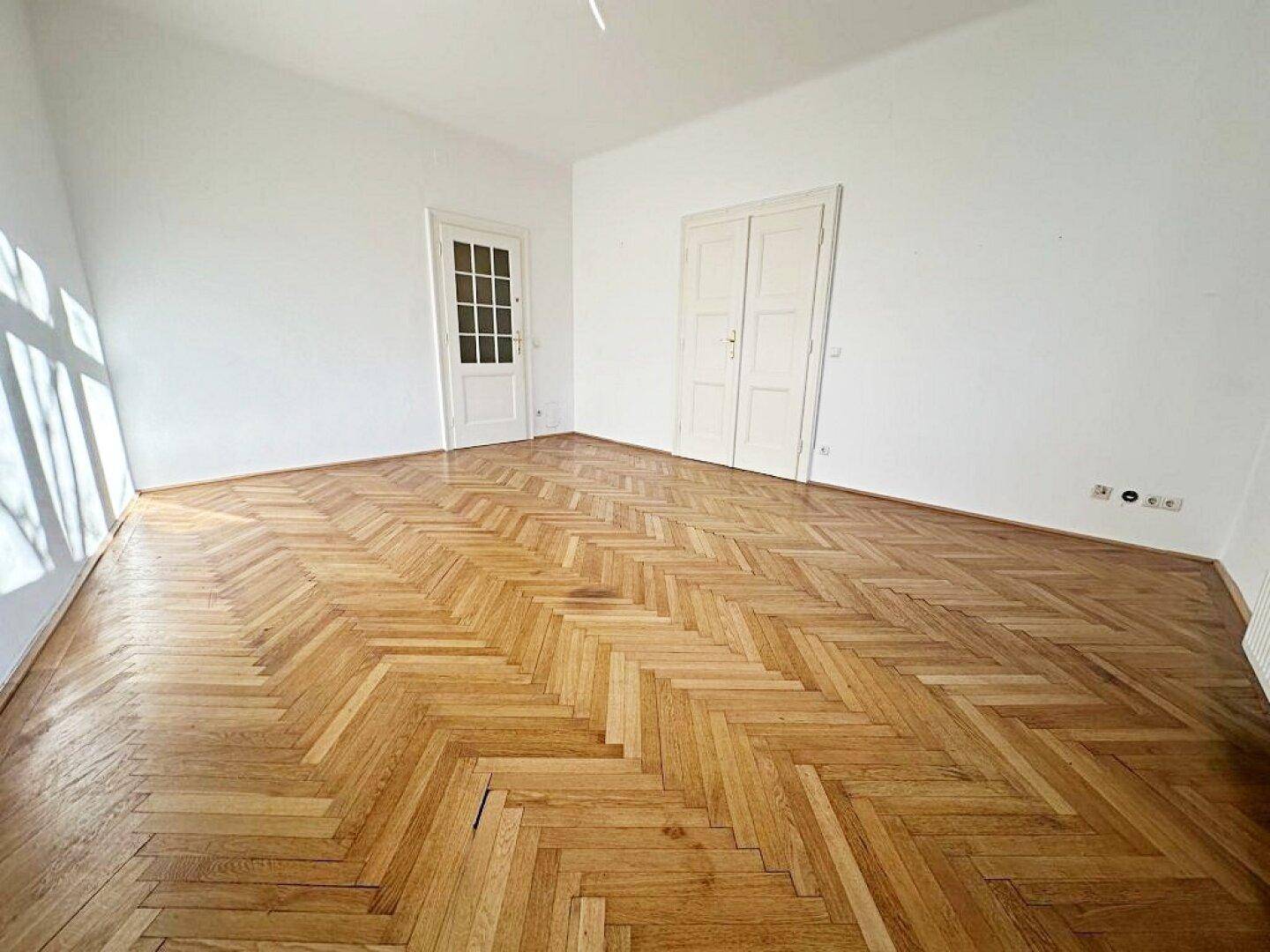 Heller Raum mit Fischgrätparkettboden und zwei Türen, die zu anderen Bereichen führen.