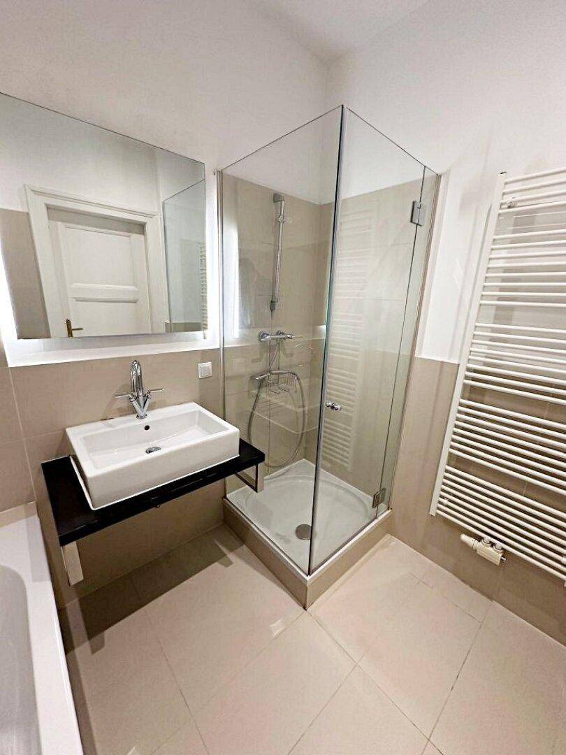 Modernes Badezimmer mit beigen Fliesen, Glasdusche, Waschbecken und beheiztem Handtuchhalter.