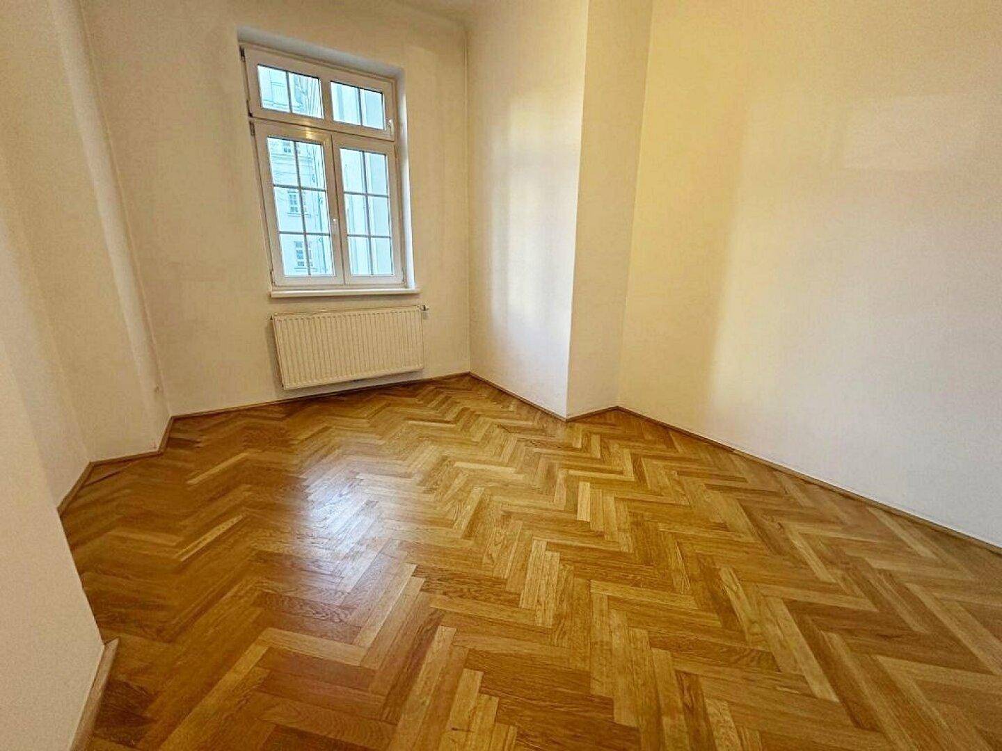 Gemütliches Zimmer mit Fischgrätparkettboden, hellen Wänden und einem Fenster für Tageslicht.