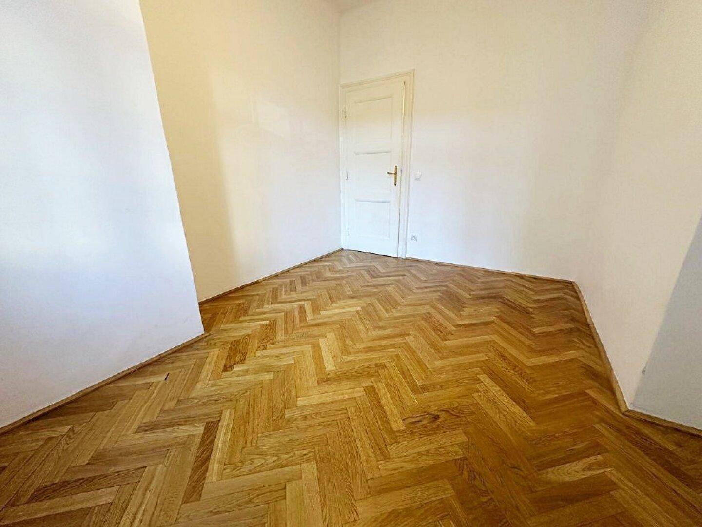 Kleiner Raum mit Fischgrätparkettboden und einer einzelnen Tür, ideal als Schlaf- oder Arbeitszimmer.