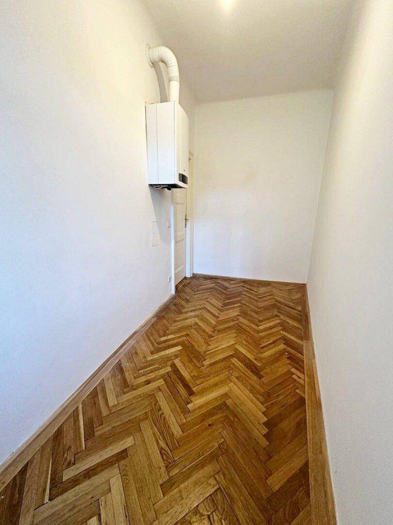 Langer Flur mit Fischgrätparkettboden und einem an der Wand befestigten Heizkessel.