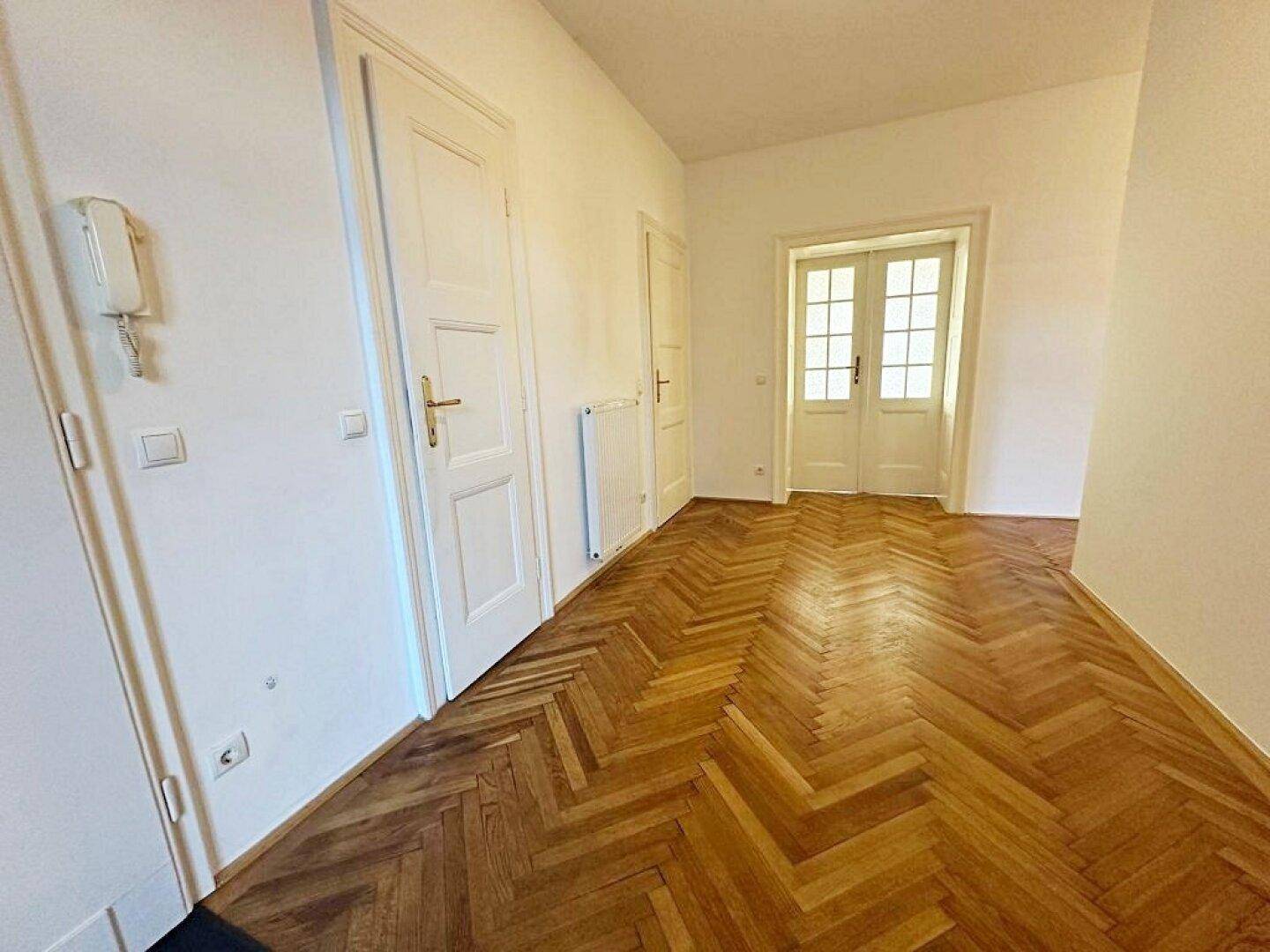 Heller Flur mit elegantem Fischgrätparkett und klassischen weißen Türen, die zu weiteren Räumen führen.