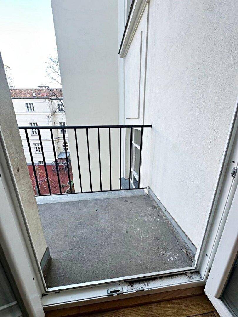 Kleiner Balkon mit schlichtem schwarzen Geländer und Blick auf die umliegenden Gebäude.
