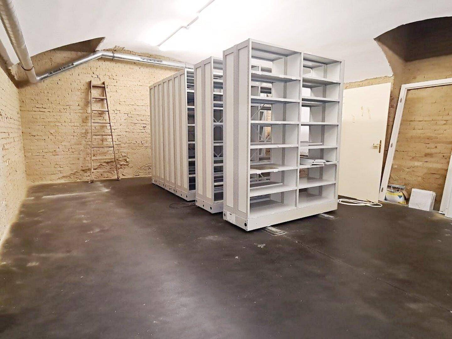Geräumiger Kellerraum mit mobilen Regalsystemen, Ziegelwänden und Betonboden, ideal für Archivierung.
