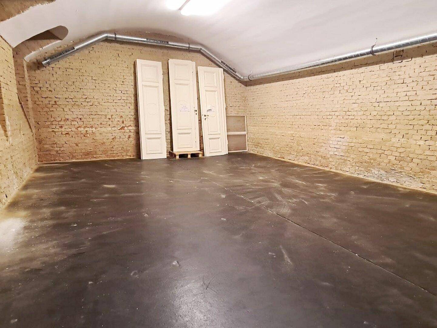 Kellerraum mit unverputzten Ziegelwänden, Betonboden und mehreren weißen Türen, die an der Wand lehnen.
