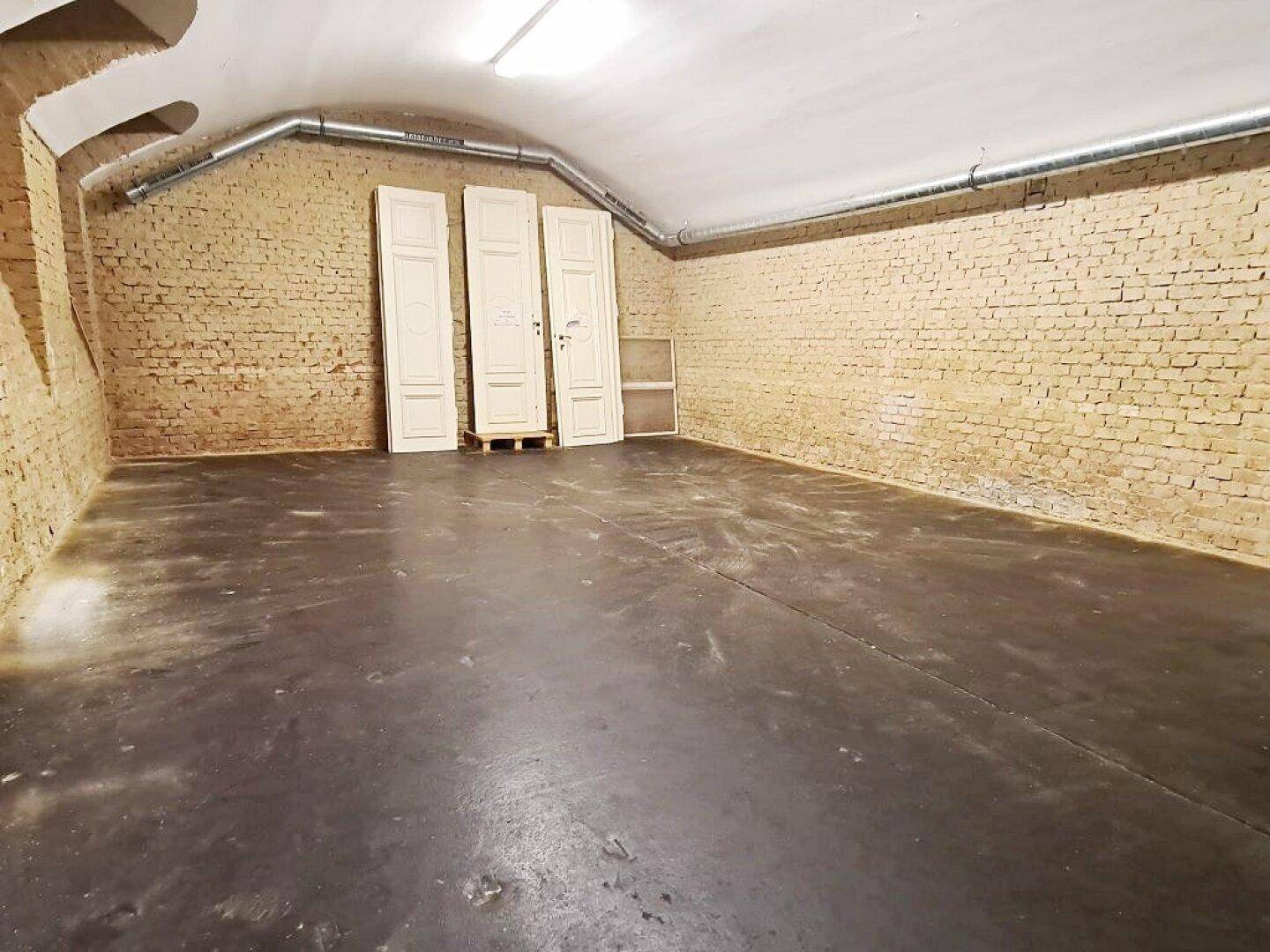 Kellerraum mit unverputzten Ziegelwänden und Betonboden, wo mehrere weiße Türen gelagert sind.