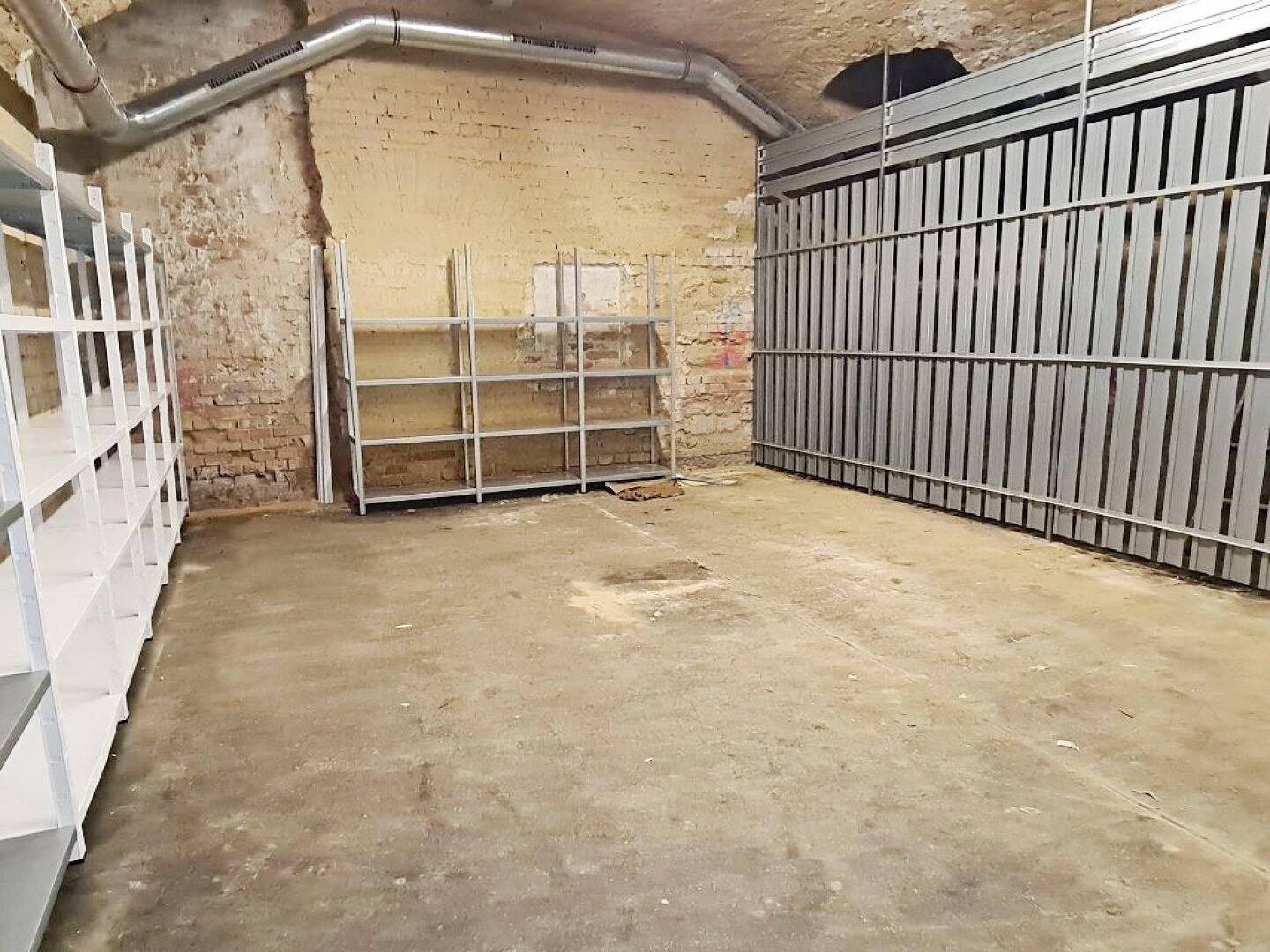 Geräumiger Kellerbereich mit freiliegenden Ziegelwänden, Metallregalen und sichtbaren Lüftungsrohren unter der Decke.