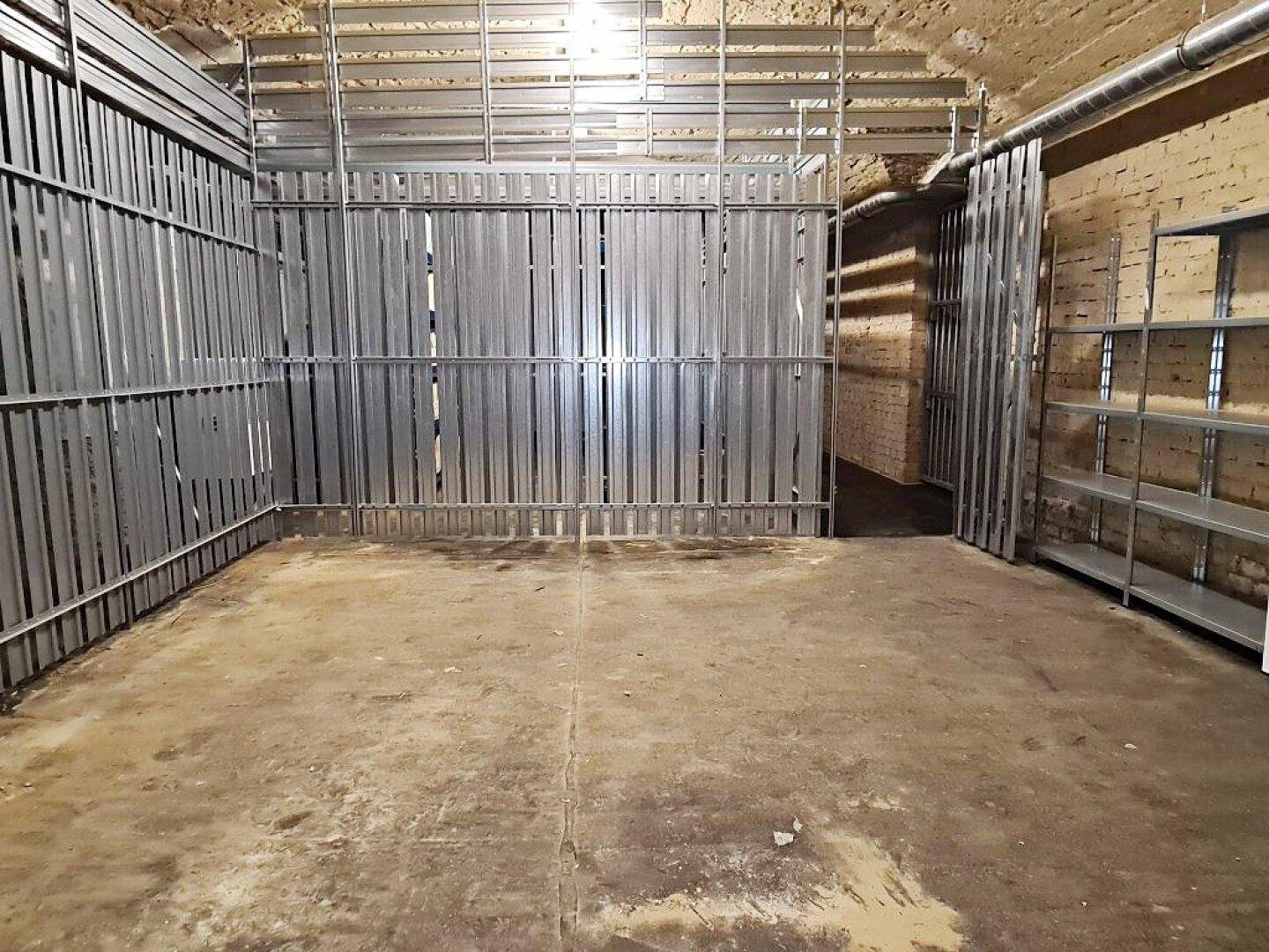 Kellerraum mit Metallabtrennungen, die separate Lagerbereiche schaffen, und einem einfachen Betonboden.
