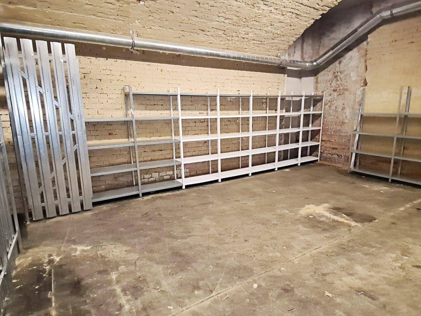 Geräumiger Kellerraum mit langen Metallregalen entlang der Ziegelwand und einem robusten Betonboden.