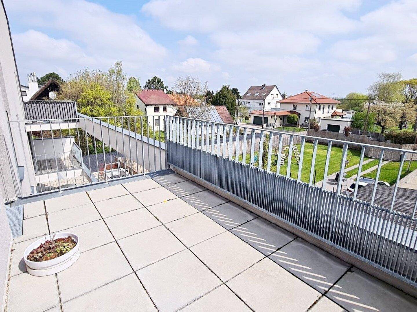 Geräumiger Balkon mit Fliesenboden und Blick auf die umliegenden Häuser und Gärten.
