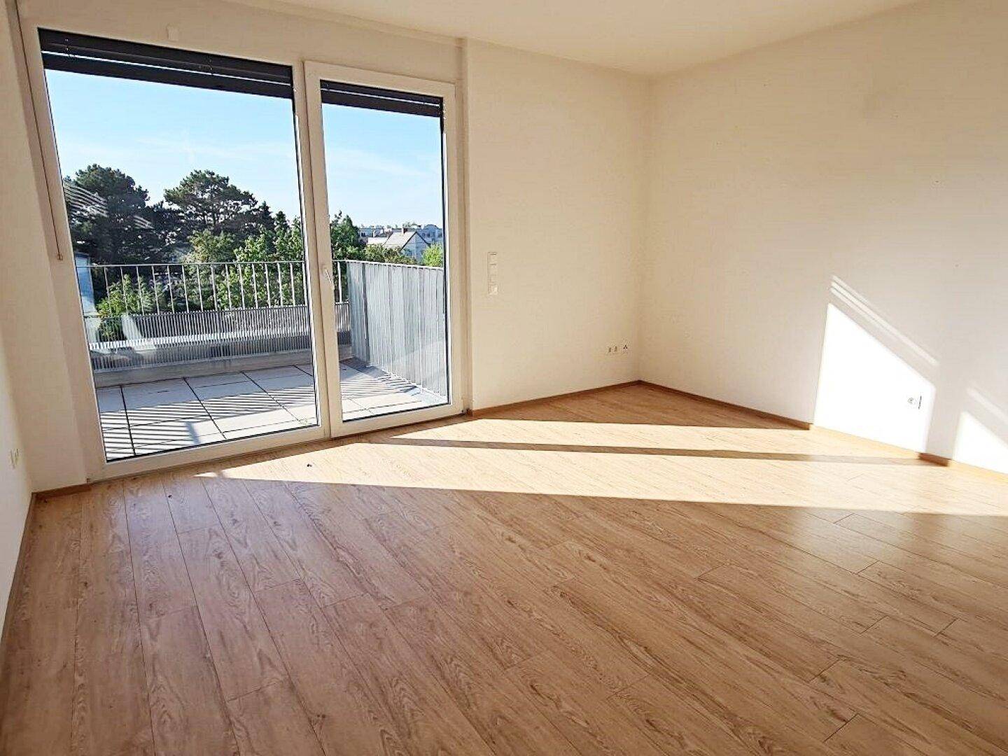 Helles Schlafzimmer mit Laminatboden und großer Fensterfront, die auf einen Balkon führt.