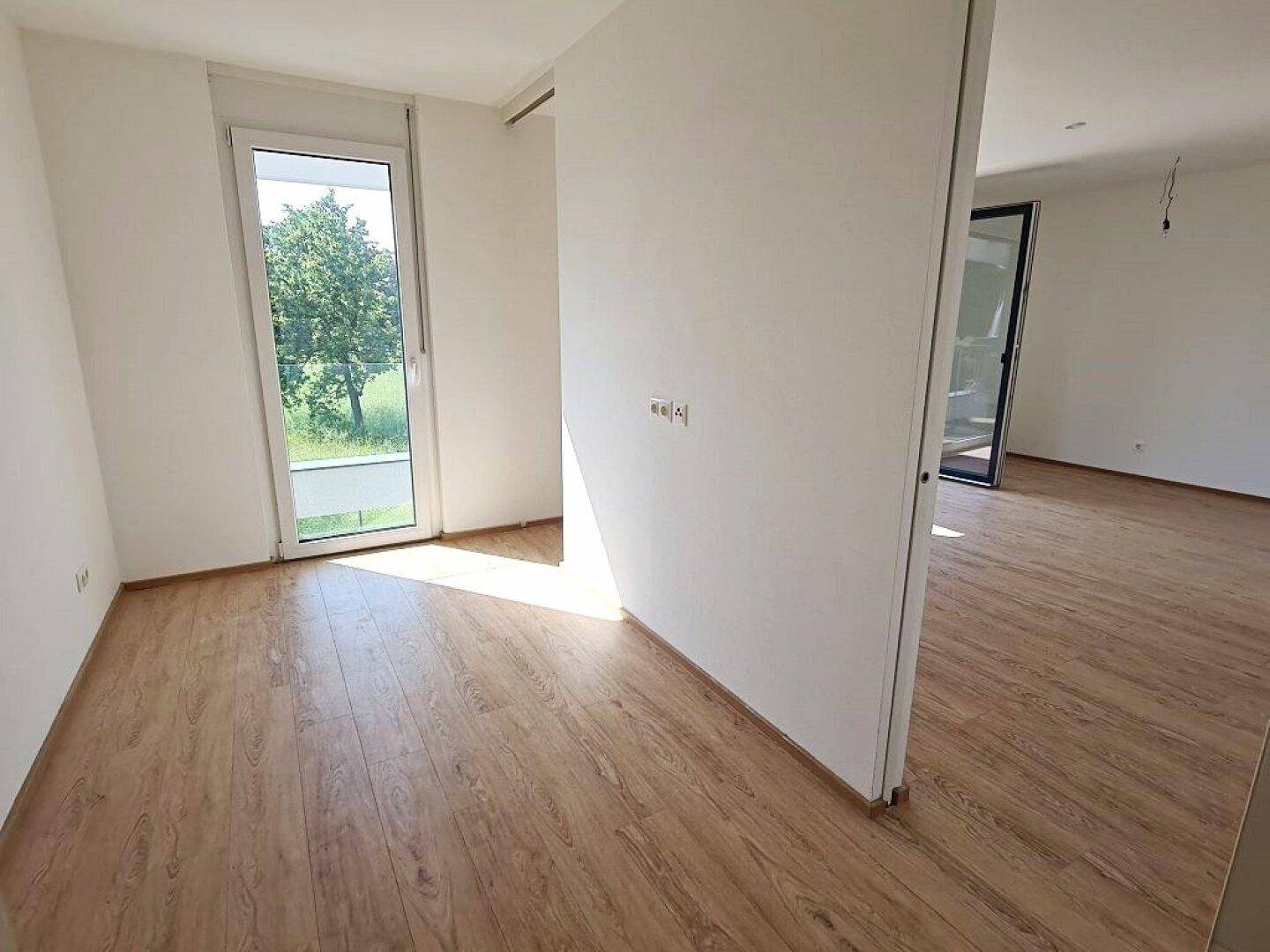 Helles Zimmer mit Laminatboden und Zugang zu einem Außenbereich, ideal als Schlaf- oder Arbeitszimmer.