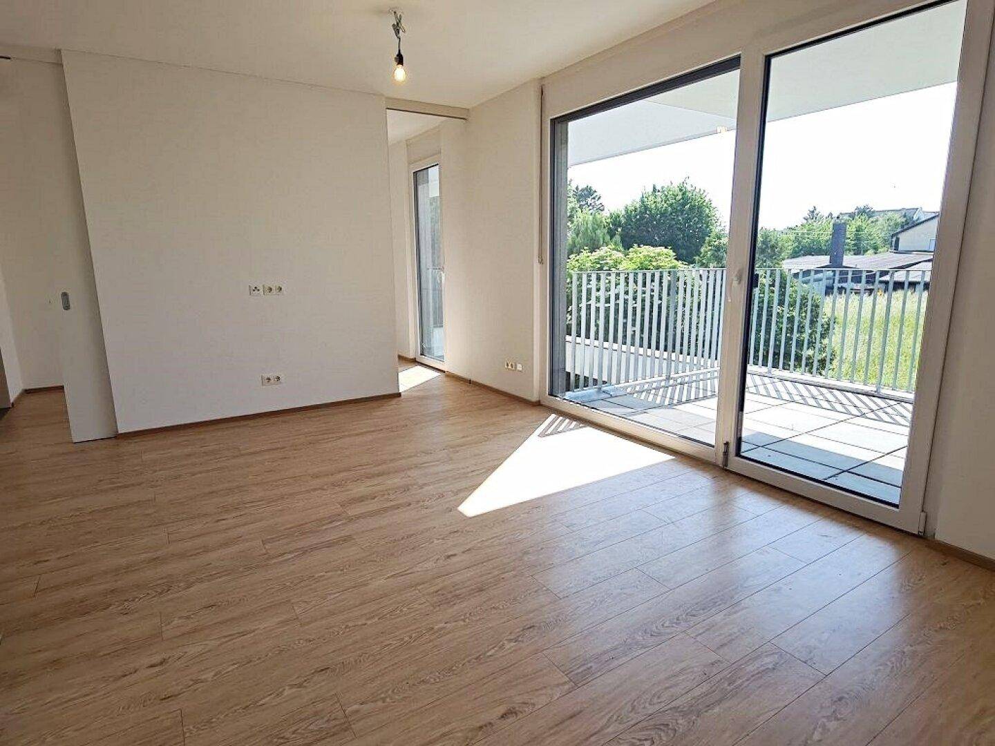 Heller Wohnraum mit Laminatboden und großen Fenstern, die Zugang zu einem Balkon bieten.