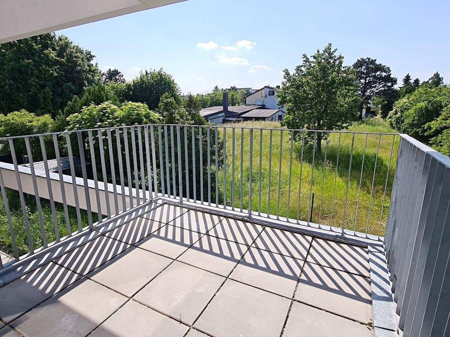 Sonniger Balkon mit Fliesenboden und Blick auf grüne Flächen und die Nachbarschaft.