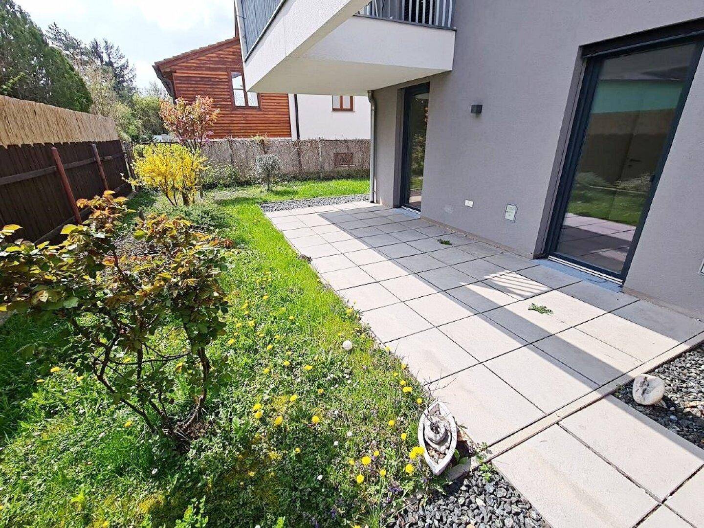 Terrasse mit Zugang zum Garten, umgeben von Grünflächen und blühenden Pflanzen.