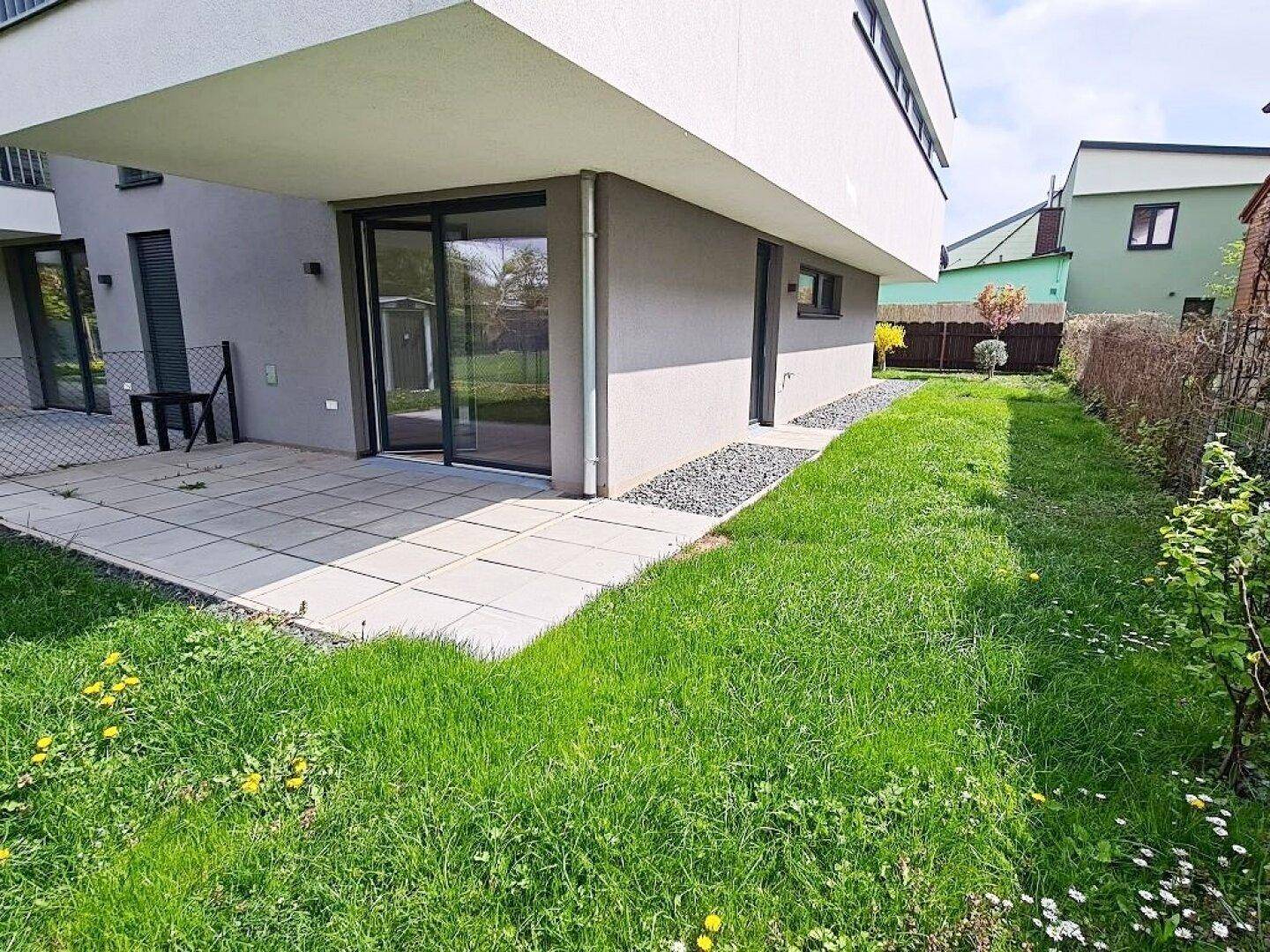 Gepflegter Gartenbereich mit Rasenfläche und einer gepflasterten Terrasse direkt am Gebäude.