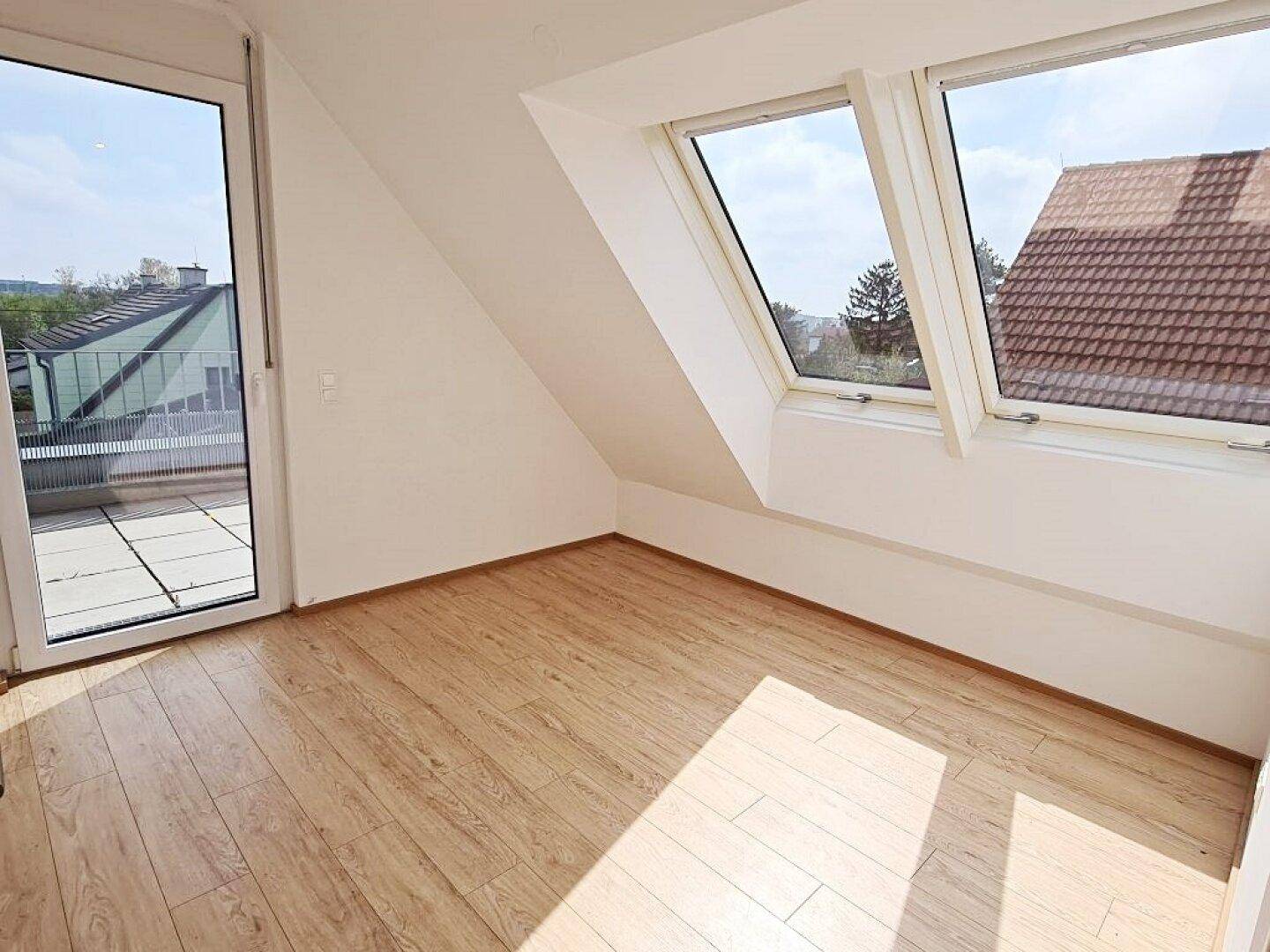 Helles Zimmer im Dachgeschoss mit Laminatboden, Dachschrägen und Zugang zu einem Balkon.