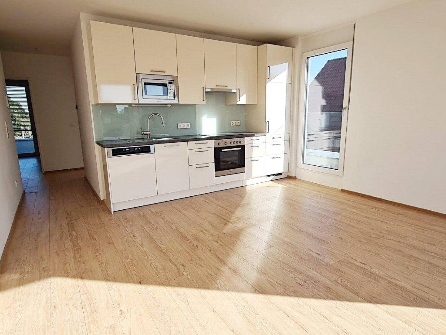 Helle, moderne Einbauküche mit weißen Hochglanzfronten und Holzboden in einem offenen Wohnbereich.
