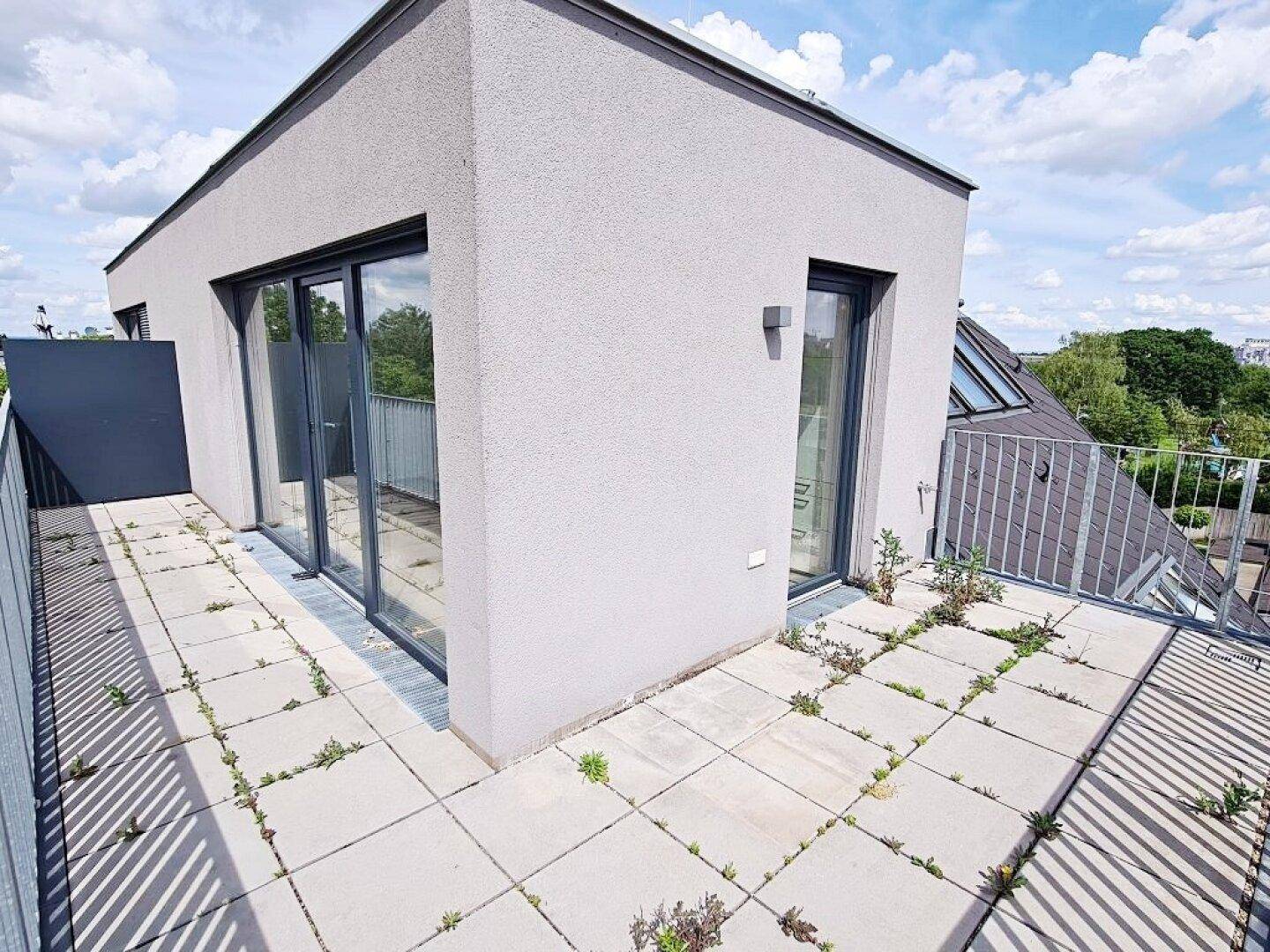 Weitläufige Dachterrasse mit Fliesenboden und angrenzendem Gebäudeteil unter blauem Himmel.