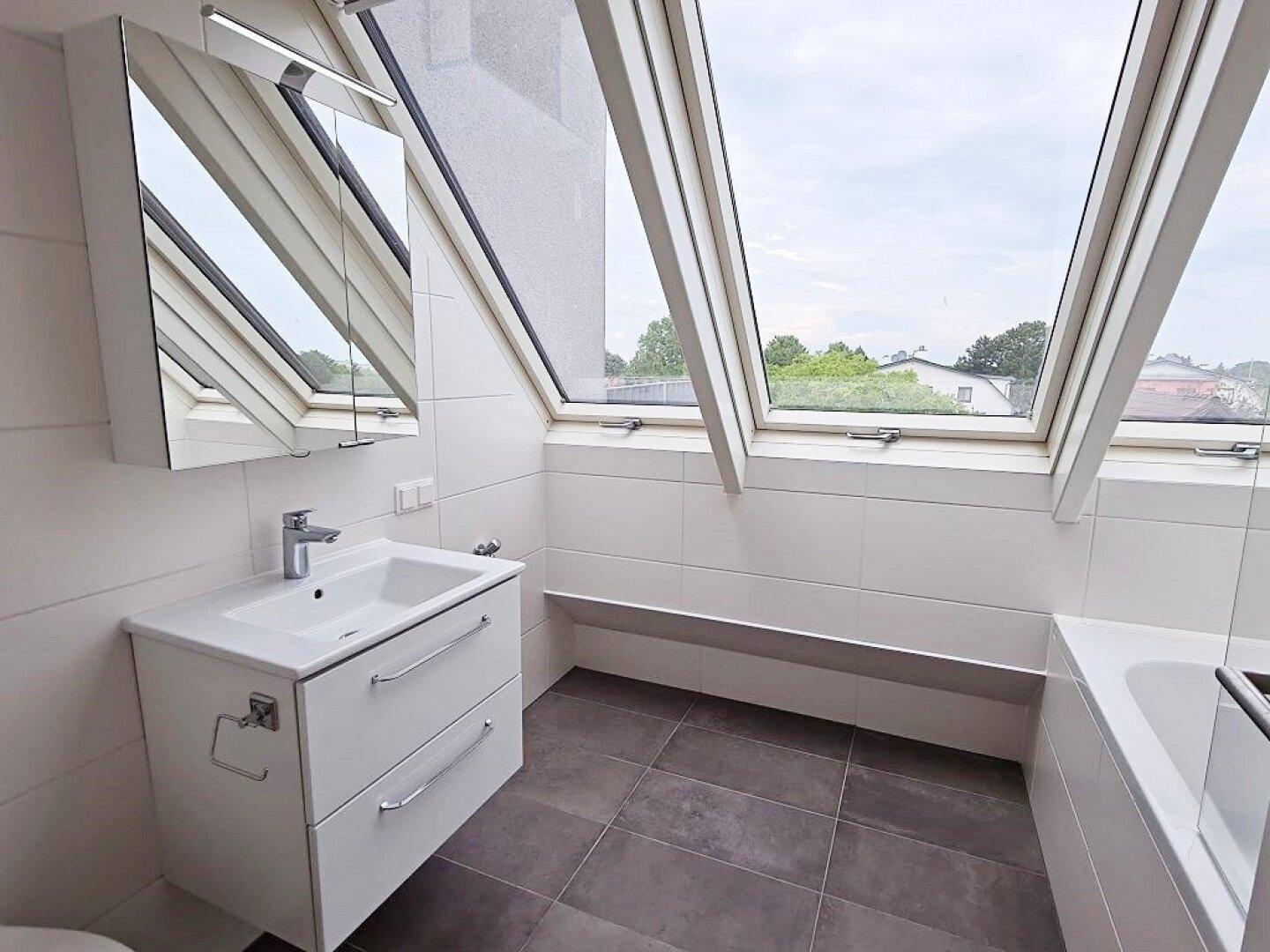Modernes Badezimmer mit Dachfenstern, Waschtisch und Badewanne unter der Dachschräge.