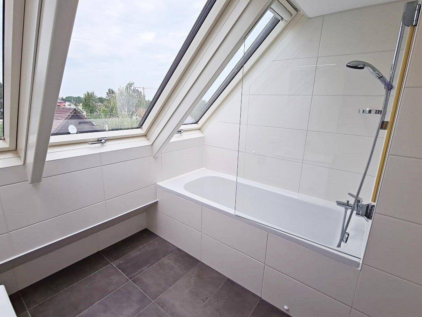Helle Badewanne mit Duschabtrennung und Dachfenstern in einem modernen Badezimmer.