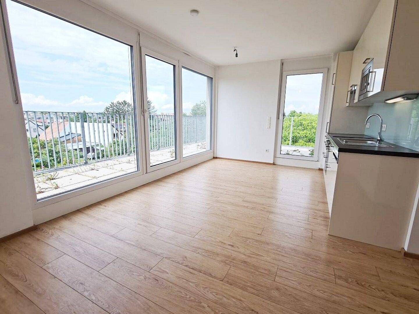 Heller Wohnbereich mit offener Küche, Laminatboden und großen Fenstern mit Zugang zur Terrasse.