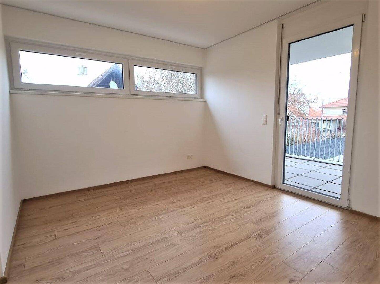 Schlafzimmer mit Laminatboden, einem Fenster und einer Tür, die auf einen Balkon führt.