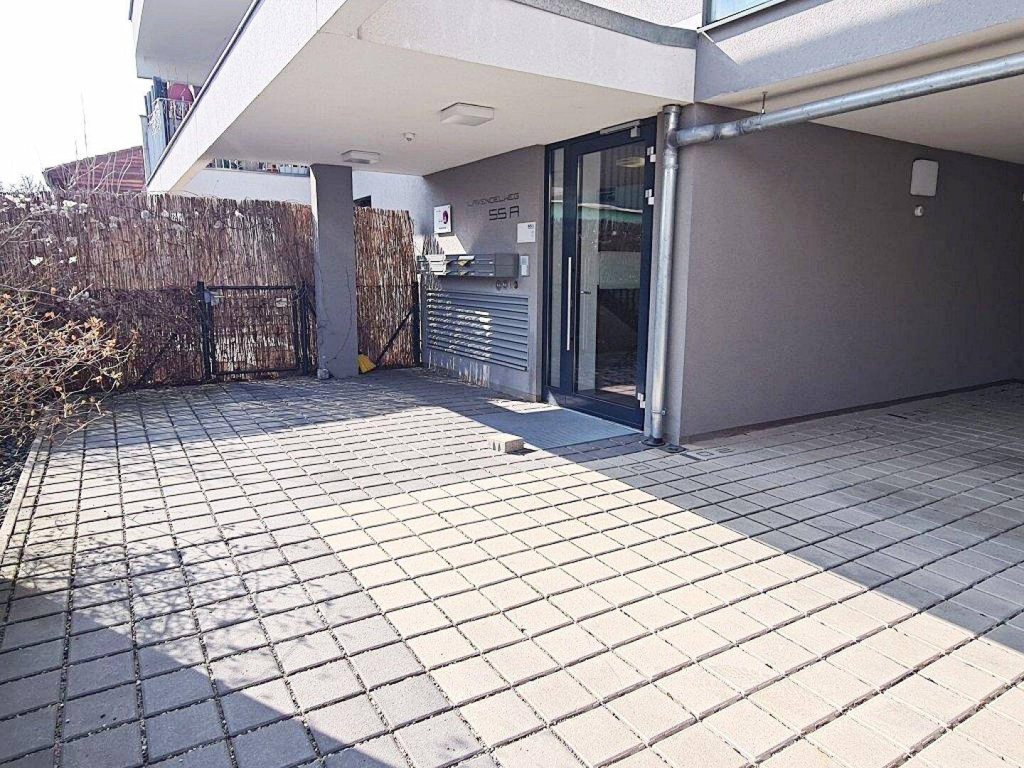 Eingangsbereich eines modernen Wohngebäudes mit gepflastertem Vorplatz und Zugangstür.