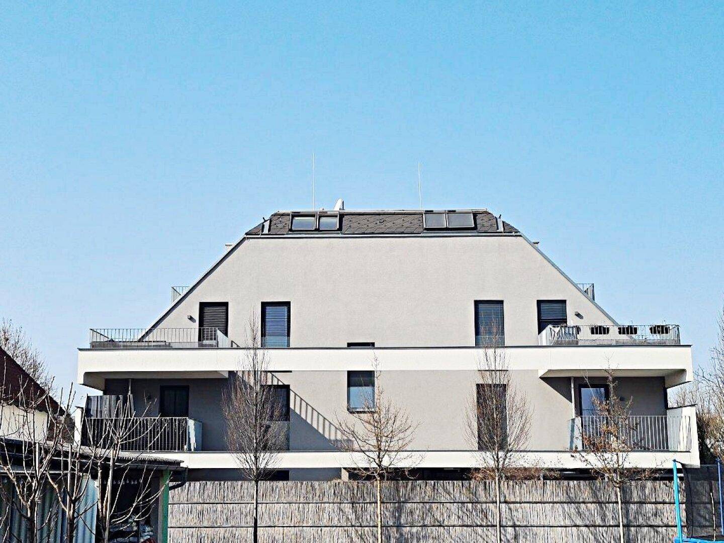 Moderne Gebäudefassade mit markantem Dach, Balkonen und großen Fenstern unter blauem Himmel.