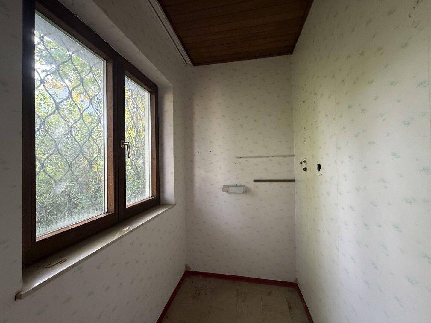 Kleiner Raum mit Fenster, Holzbalkendecke und einfacher Tapete, bereit für die Renovierung.