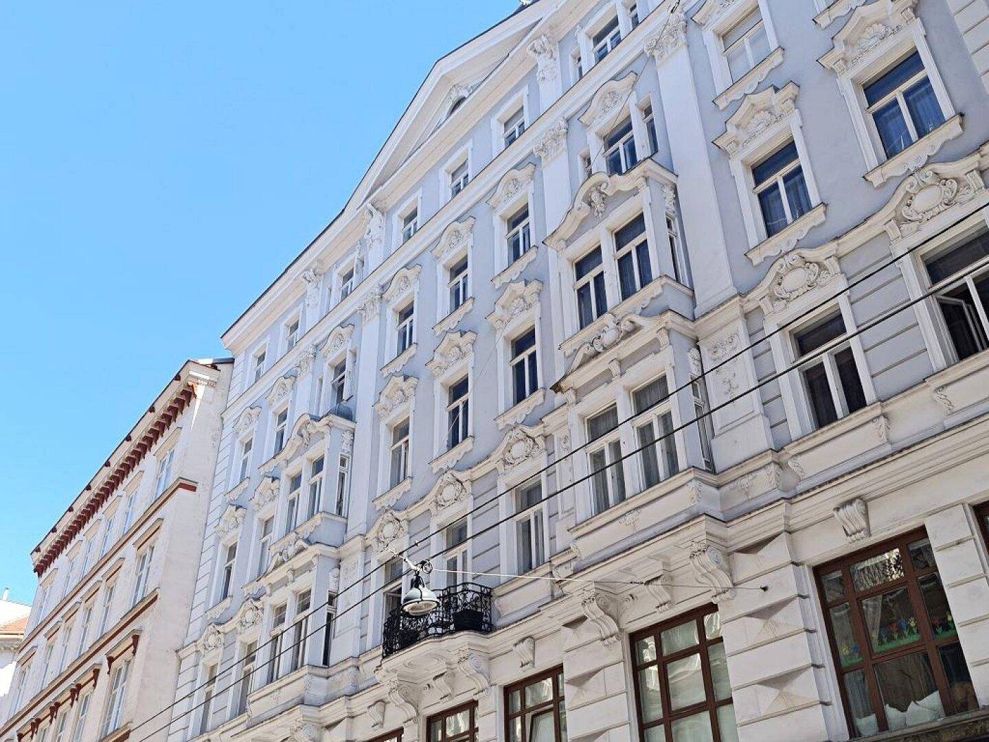Historisches Gebäude mit reich verzierter Fassade, vielen Fenstern und kleinen Balkonen unter blauem Himmel.