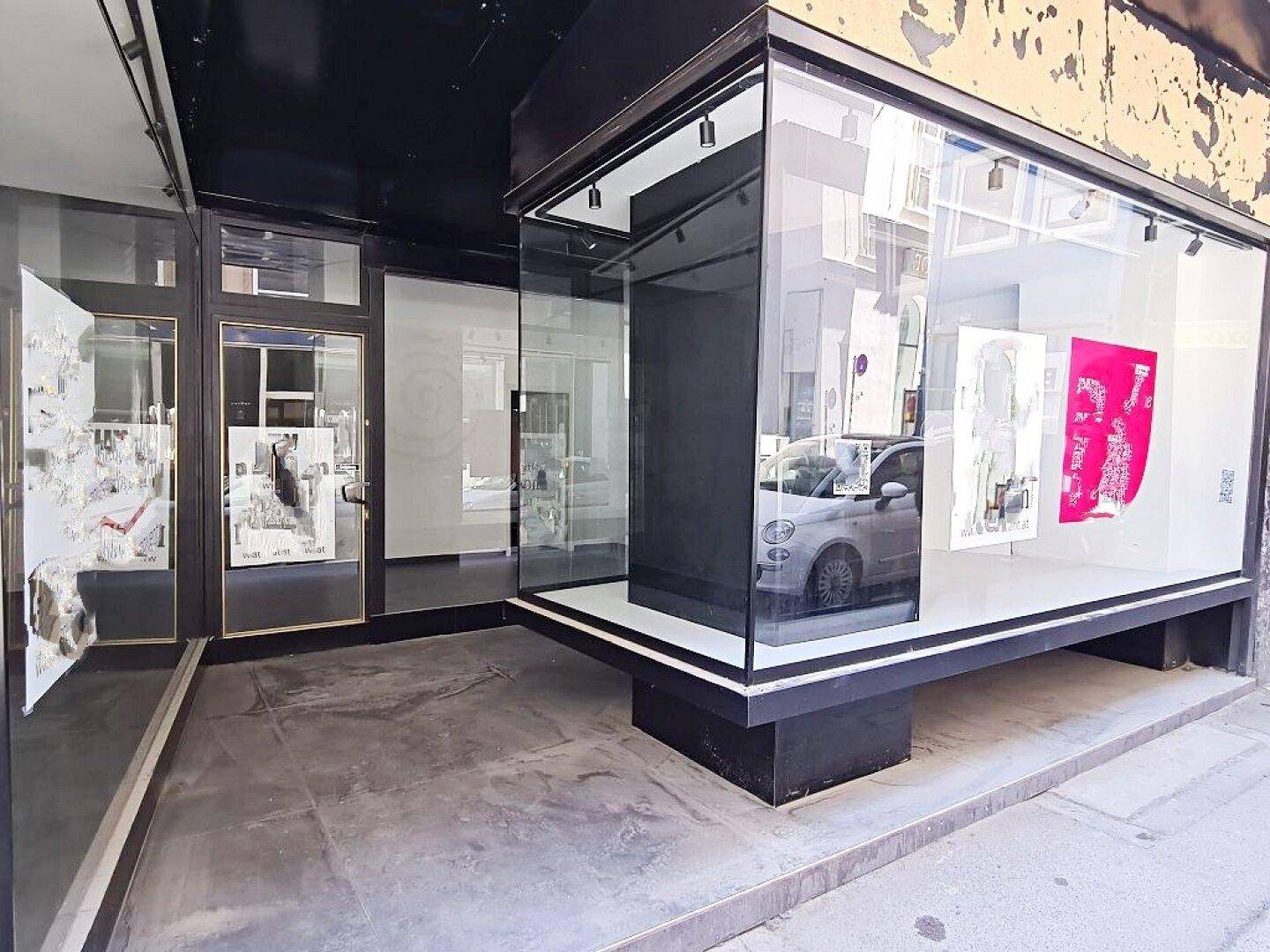 Moderne Ladenfassade mit großen Schaufenstern und Ausstellungsfläche, die das Straßenbild widerspiegelt.