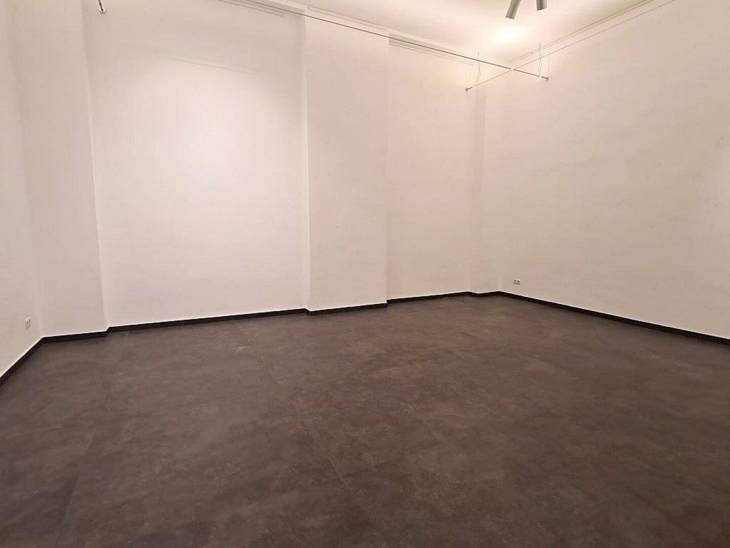 Leerer Geschäftsraum mit weißen Wänden und dunklem Fliesenboden, bietet vielseitige Gestaltungsmöglichkeiten.