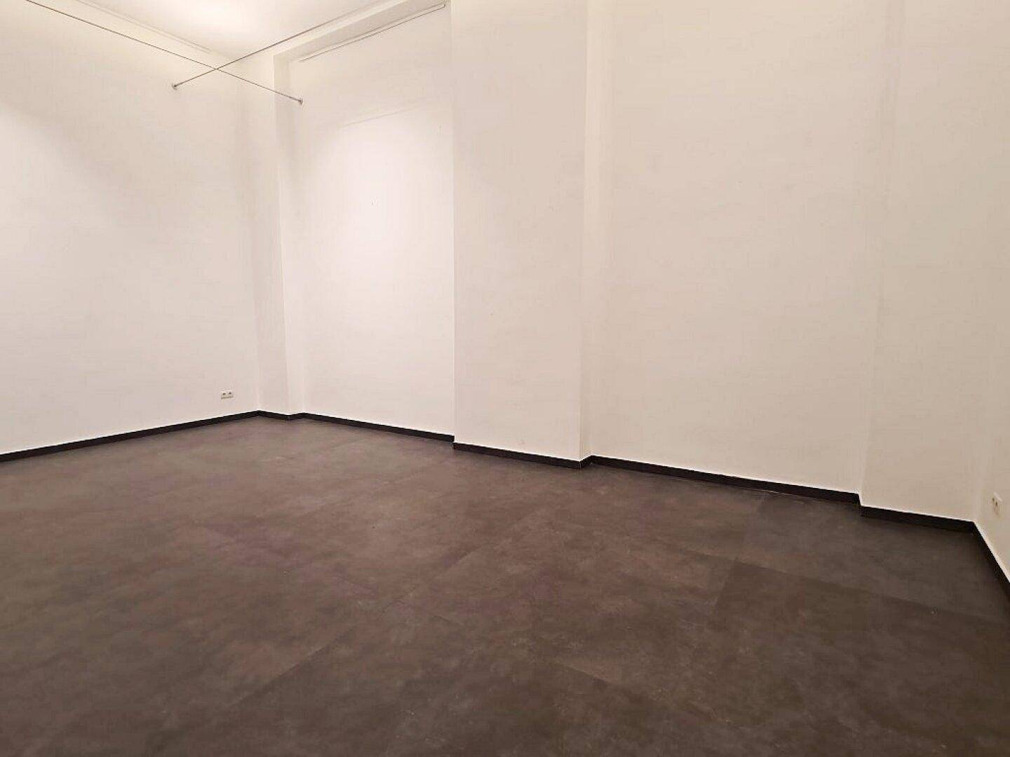 Heller, unmöblierter Ladenbereich mit weißen Wänden und dunklem Boden, ideal für flexible Nutzung.