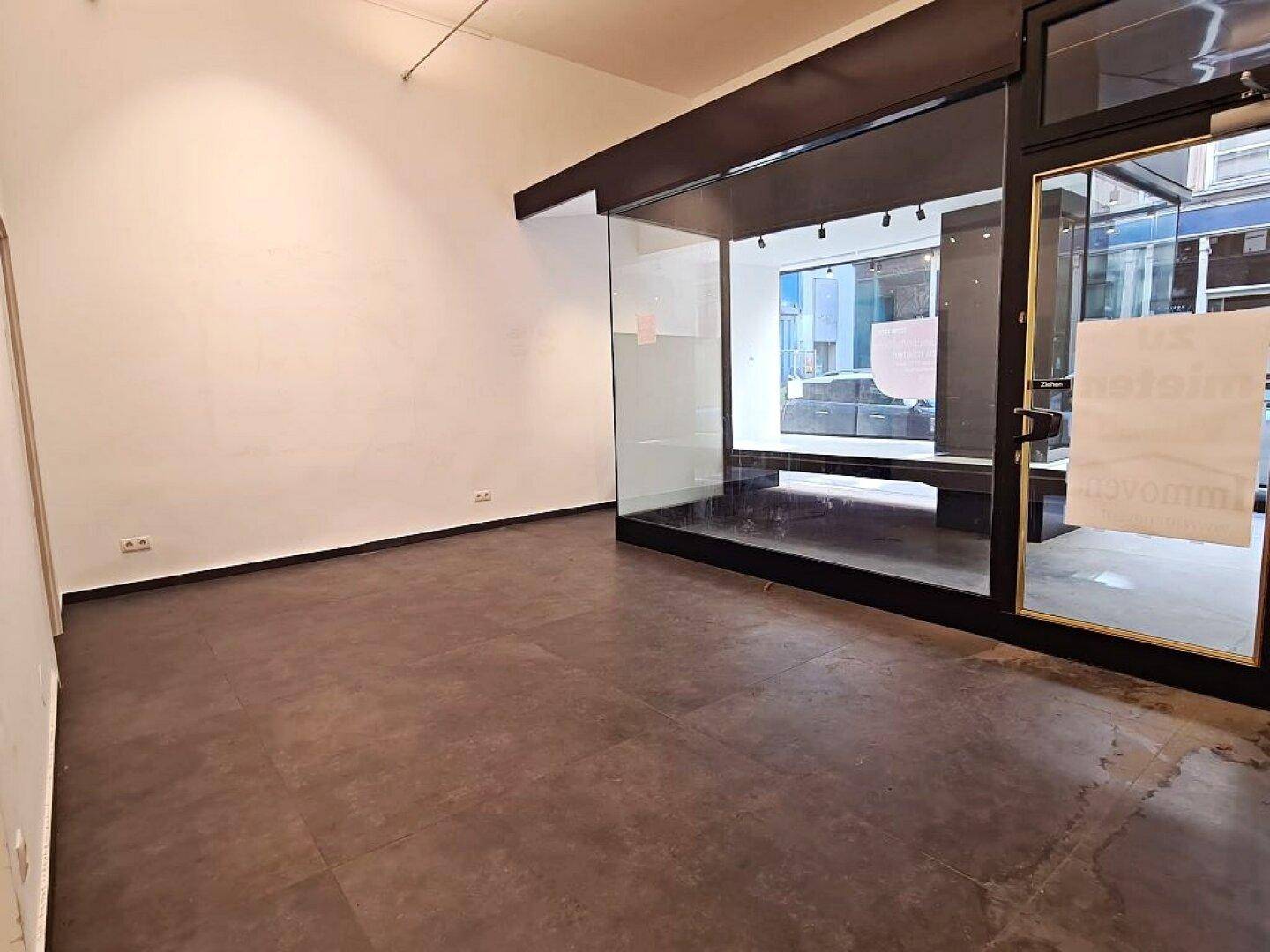 Innenansicht eines Geschäftsraums mit großzügiger Glasfront und Eingangstür, die viel Licht hereinlässt.