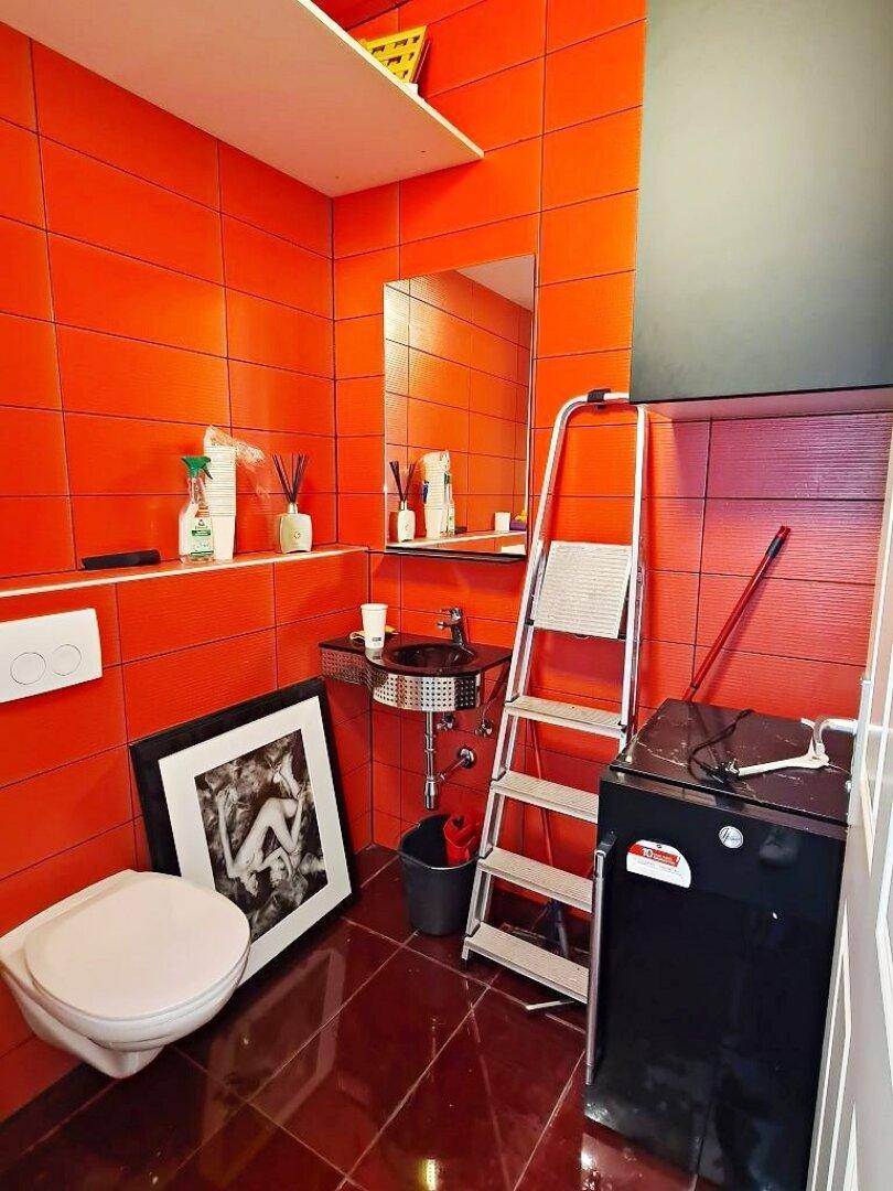 Funktionales Badezimmer mit auffälligen orangefarbenen Fliesen, Toilette, Waschbecken und einer Waschmaschine.