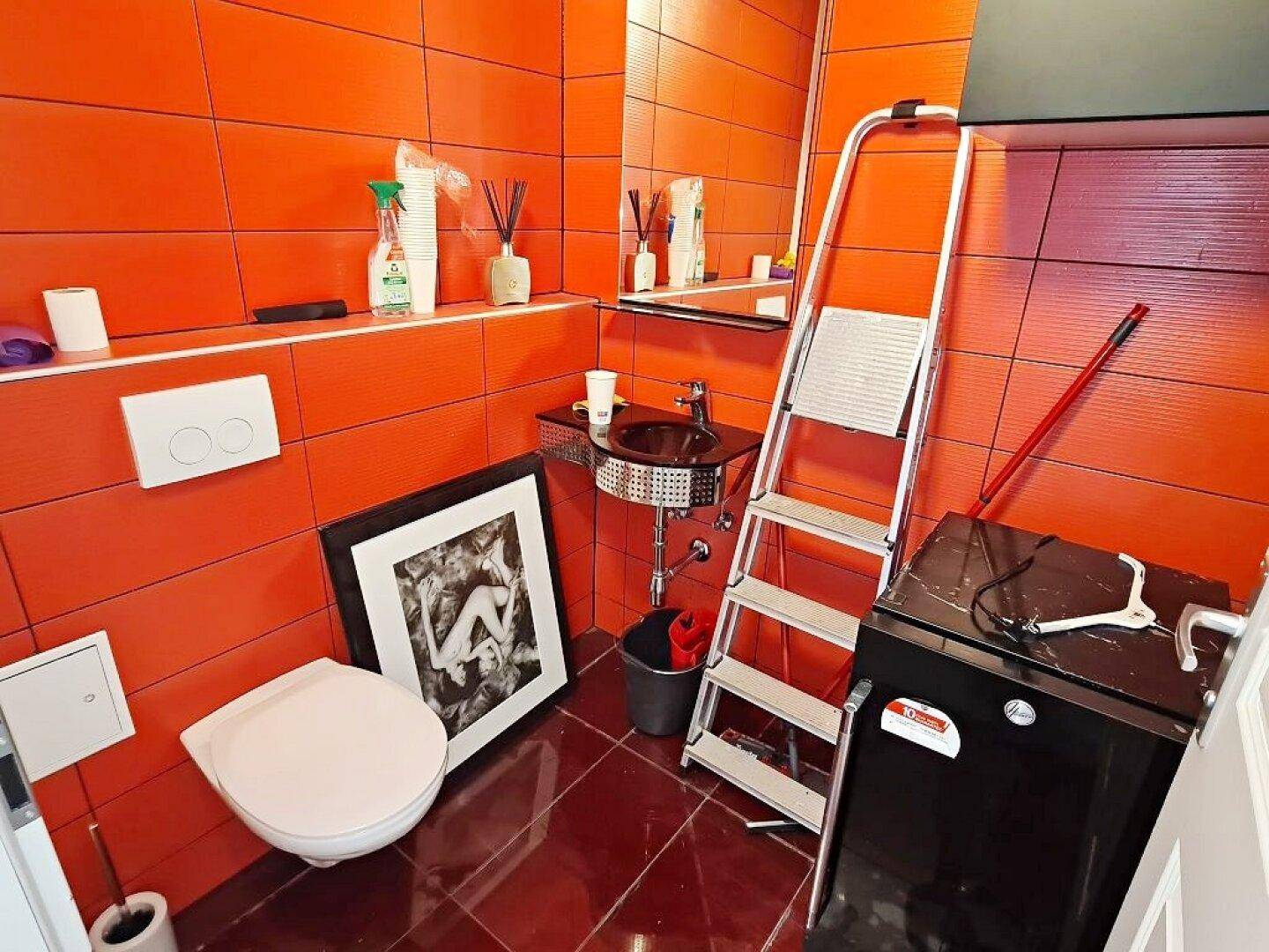Kleines Badezimmer mit leuchtend orangefarbenen Fliesen, Toilette, Waschbecken und einer Waschmaschine.