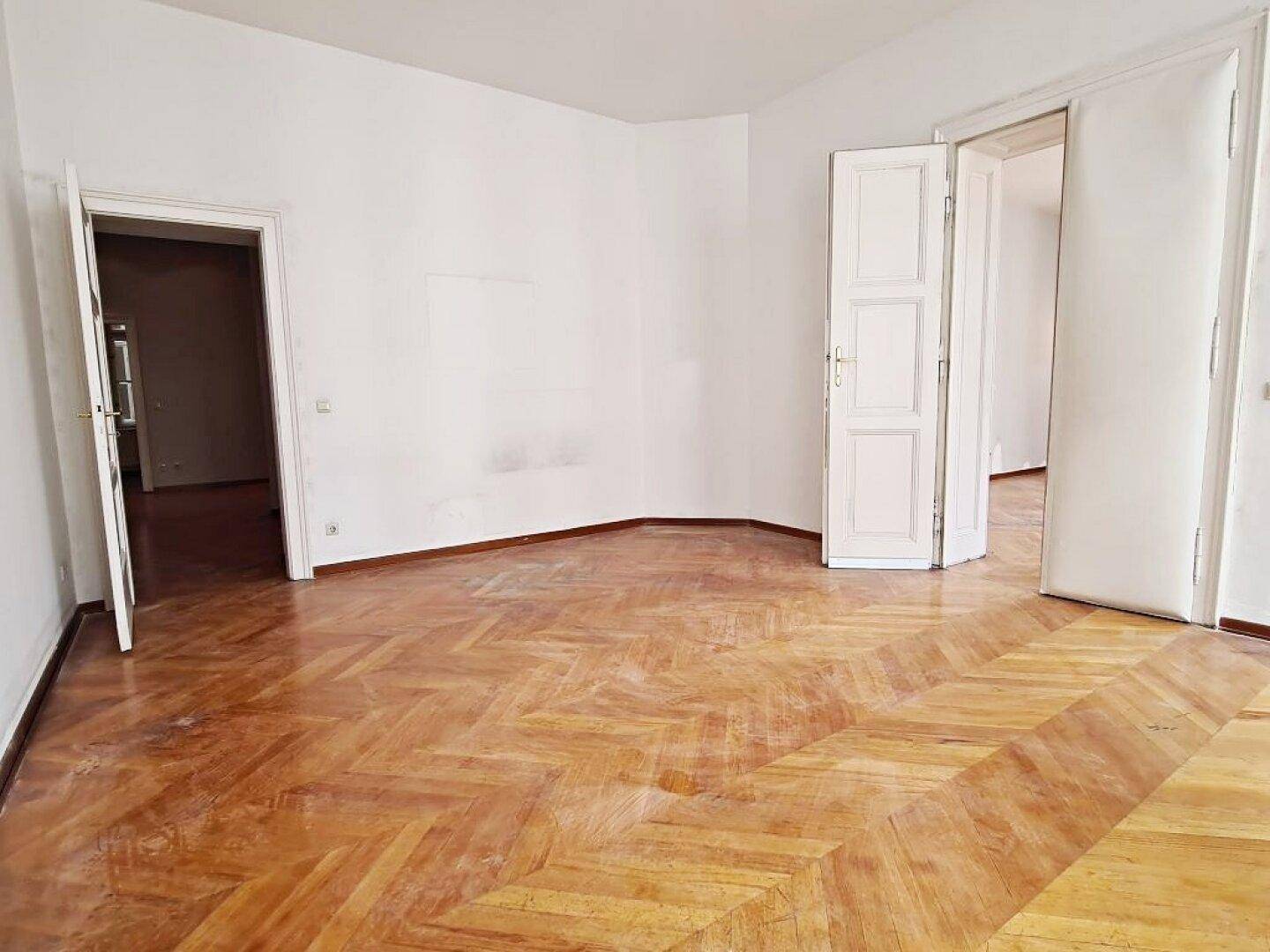 Großzügiger Raum mit elegantem Fischgrätparkett und hohen Decken, ideal für Wohn- oder Schlafzimmer.