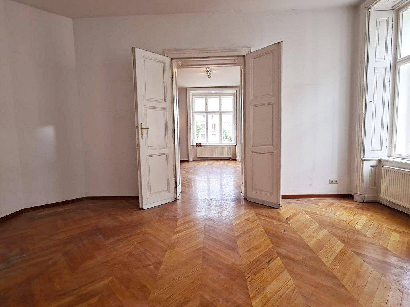 Repräsentativer Raum mit Fischgrätparkett und Doppeltüren, verbindet zwei helle Wohnbereiche.