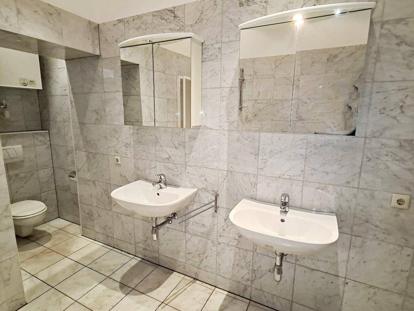 Modernes Badezimmer mit doppelten Waschbecken, Spiegelschränken und eleganten Marmorfliesen.