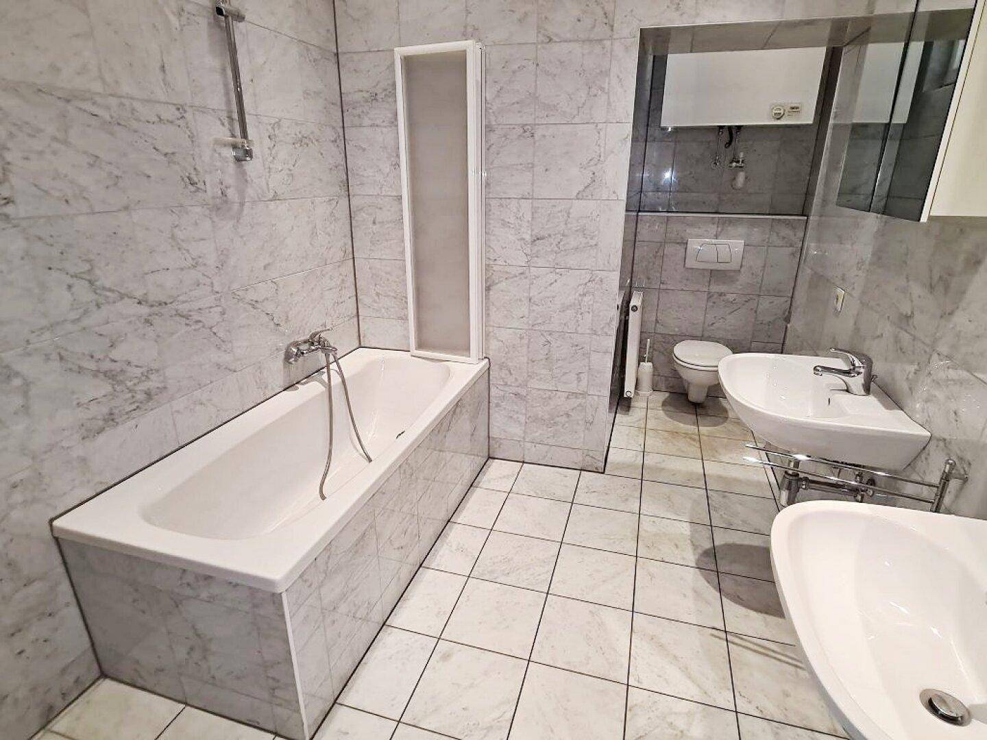 Geräumiges Badezimmer mit Badewanne, Duschabtrennung und WC, vollständig mit Marmorfliesen ausgestattet.