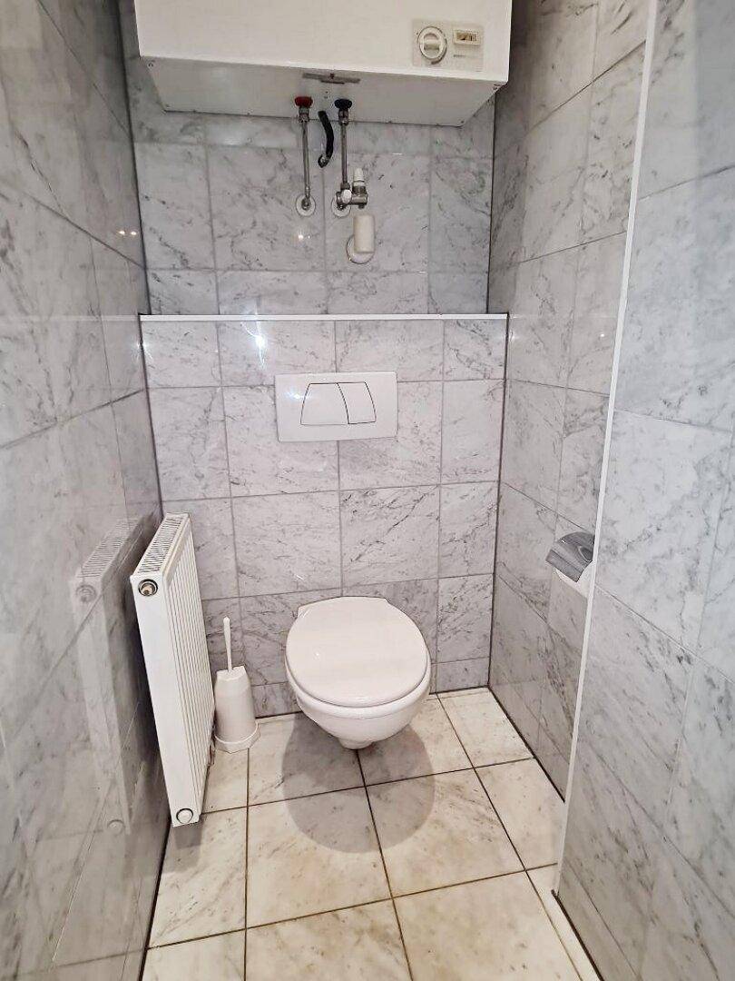 Separates WC mit wandhängender Toilette, Heizkörper und modernen Marmorfliesen.
