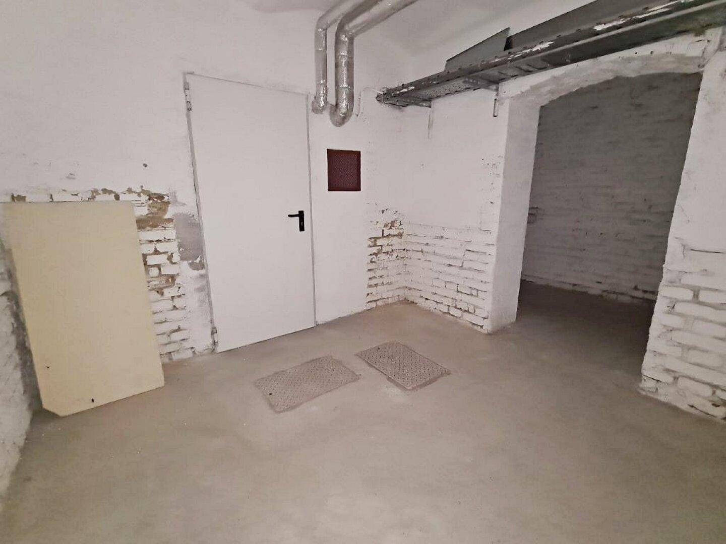 Unfertiger Kellerraum mit freigelegten Ziegelwänden, Betonboden und sichtbaren Rohren an der Decke.