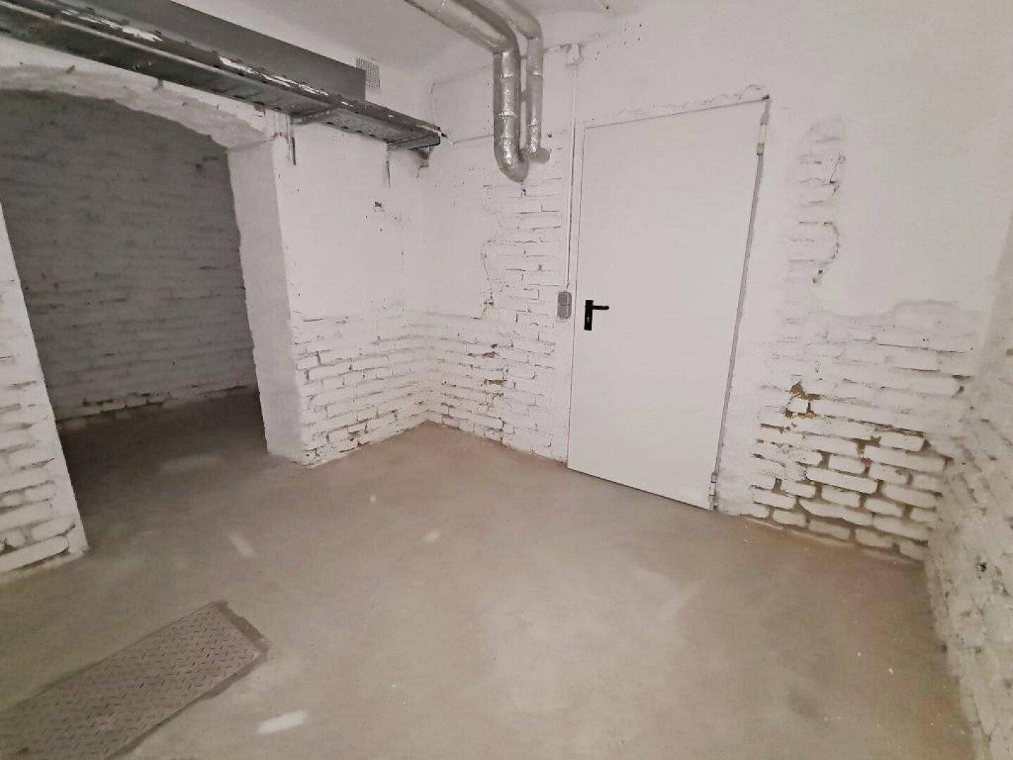 Geräumiger Kellerbereich mit weiß gestrichenen Ziegelwänden, einem Betonboden und sichtbaren Deckenrohren.