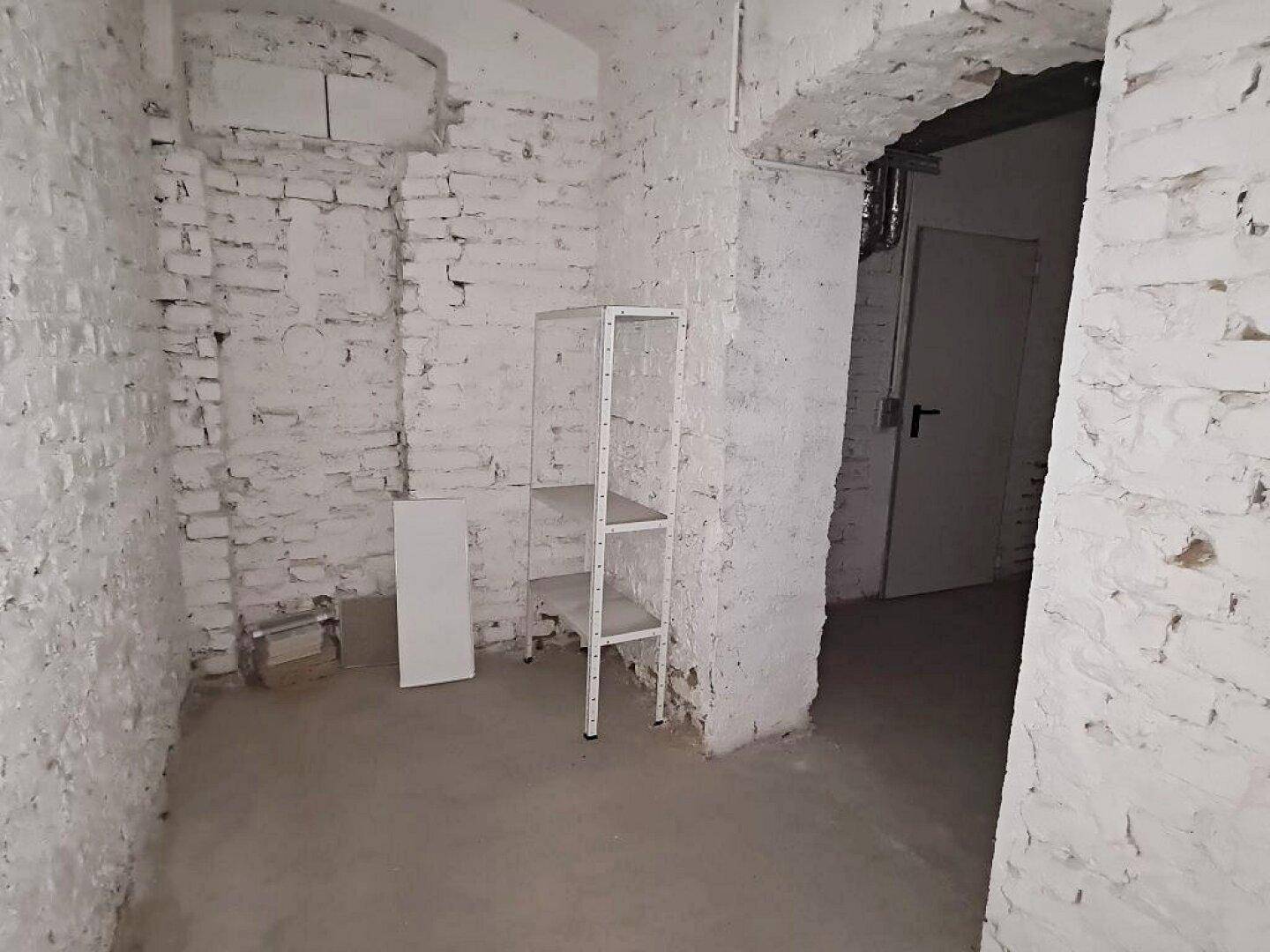 Kellerraum mit freigelegten Ziegelwänden, Betonboden und einem einfachen Metallregal für Lagerzwecke.
