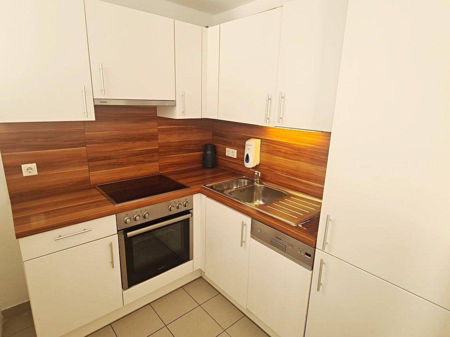 Moderne Einbauküche mit weißen Schränken, Holz-Arbeitsplatten und integrierten Elektrogeräten.
