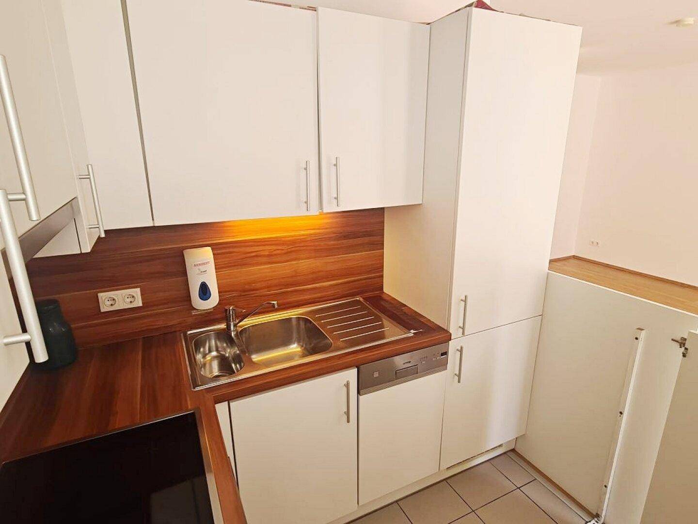 Funktionale Küche mit Spülbecken, Geschirrspüler und ausreichend Stauraum in den weißen Oberschränken.