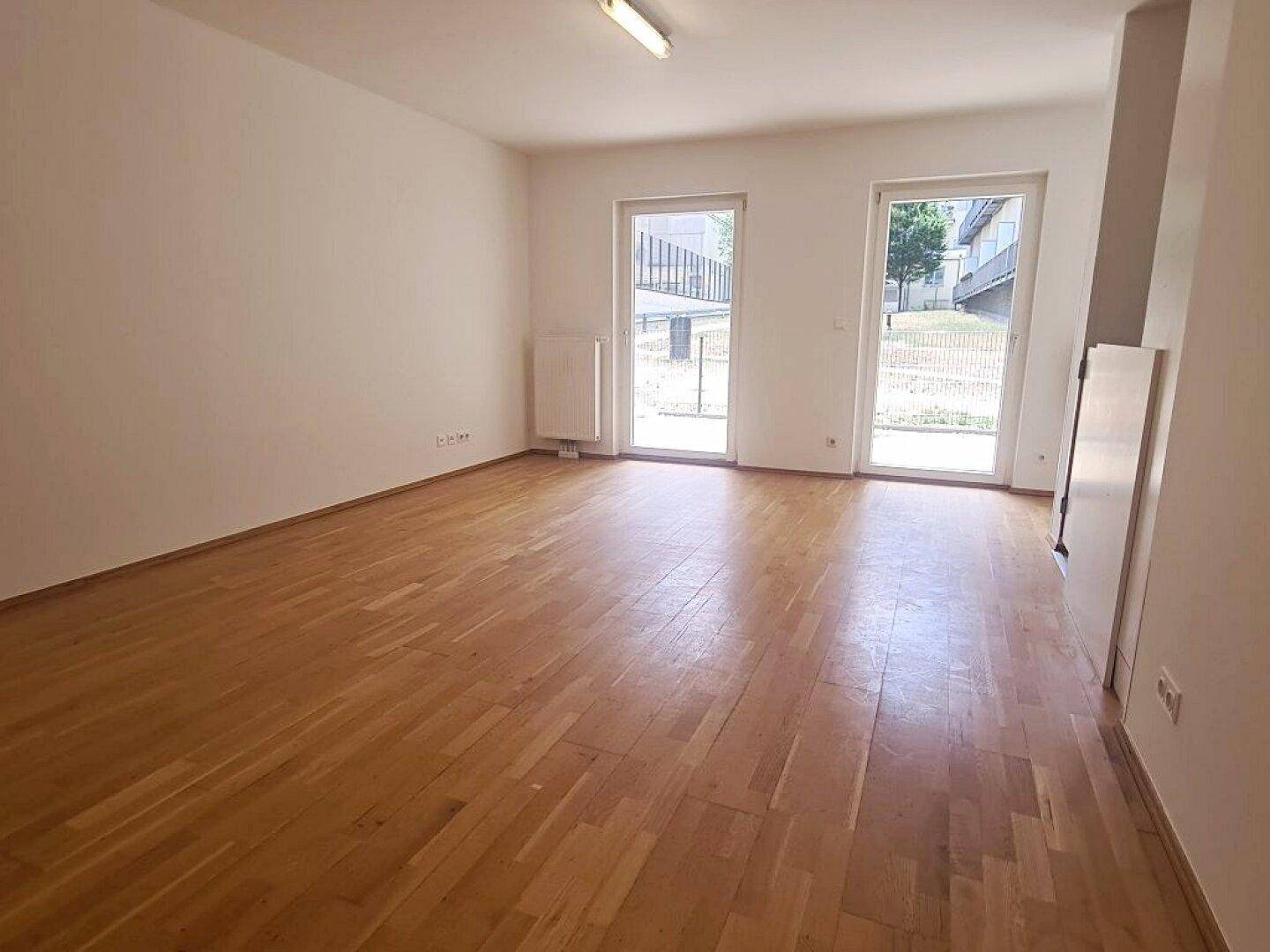 Lichtdurchfluteter Wohnbereich mit Parkett und zwei großen Fenstertüren, die ins Freie führen.