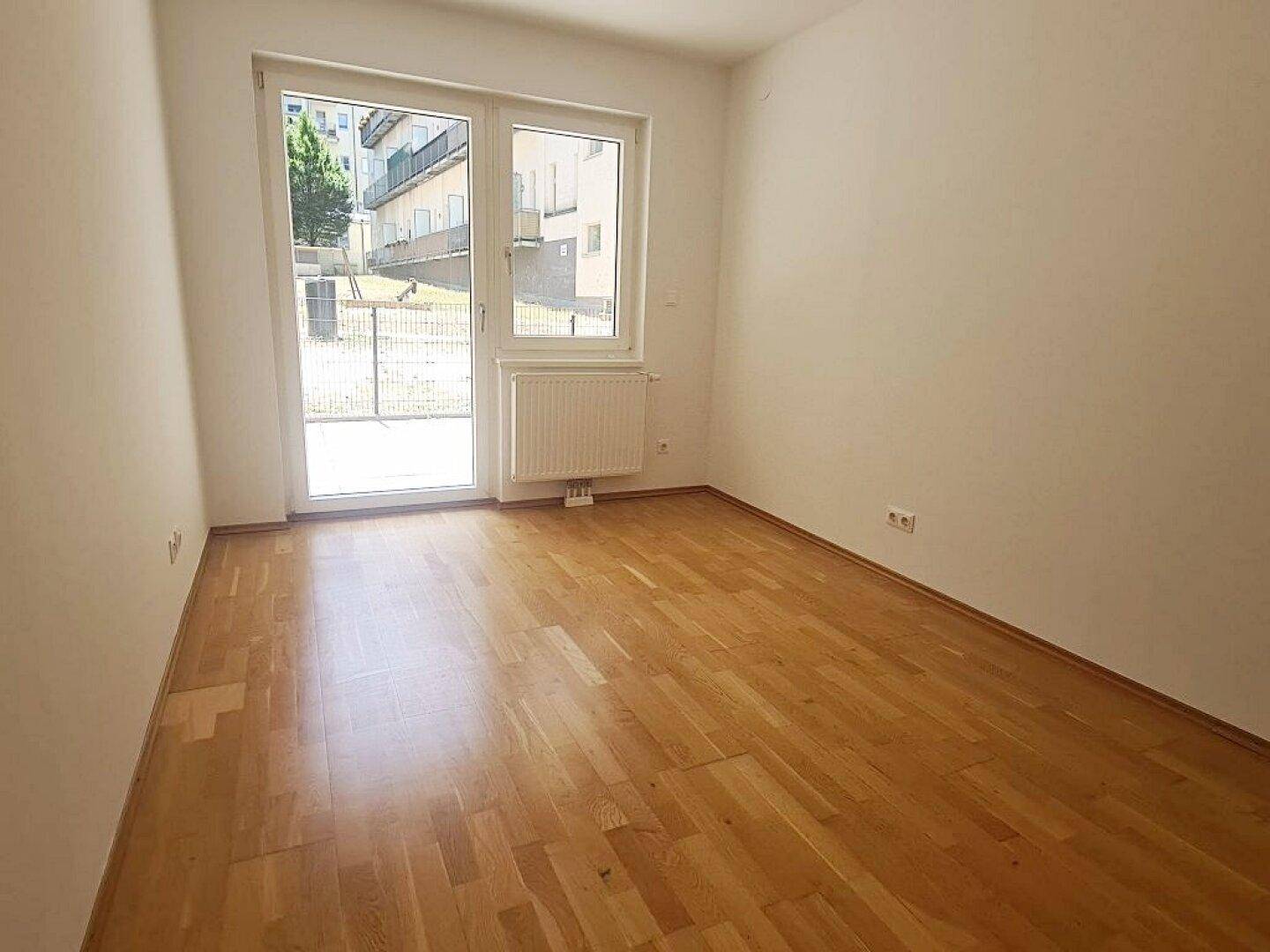 Helles Schlafzimmer mit Parkettboden und großem Fenster, das viel Tageslicht hereinlässt.