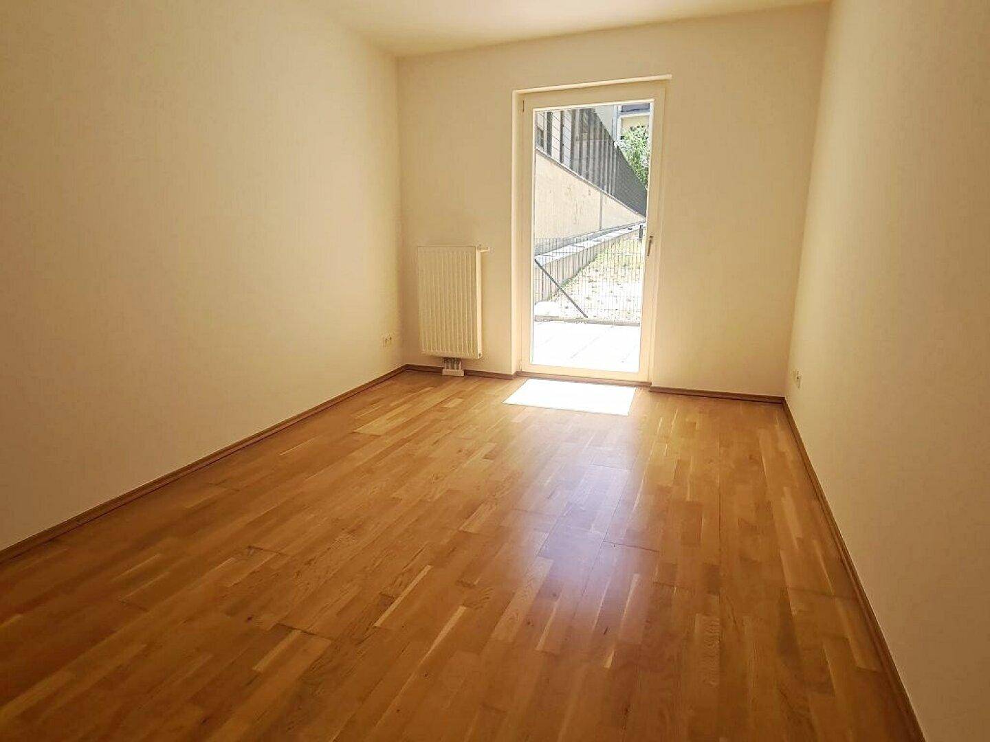 Freundliches Zimmer mit Parkettboden und Fensterfront, die den Raum mit Licht erfüllt.
